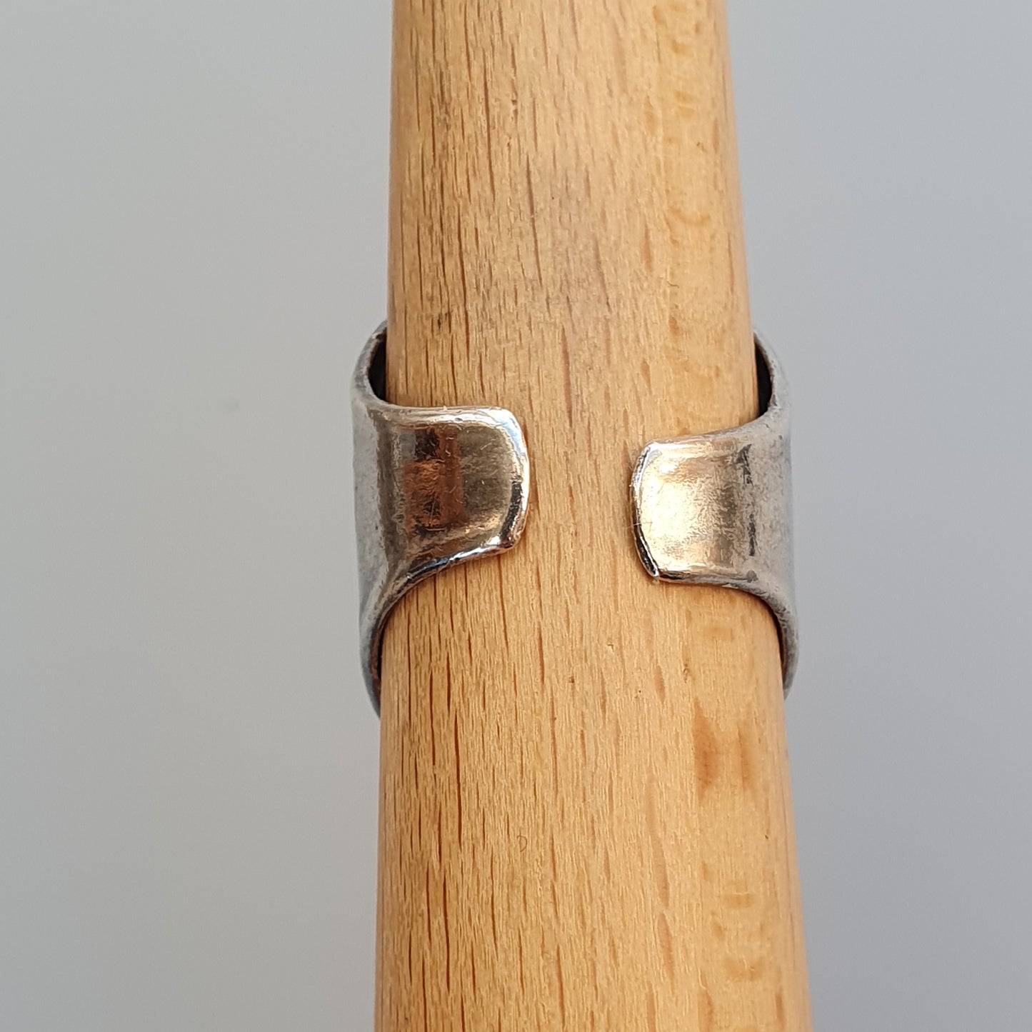 Silver ring with an open design wrapped around a wooden cylinder.