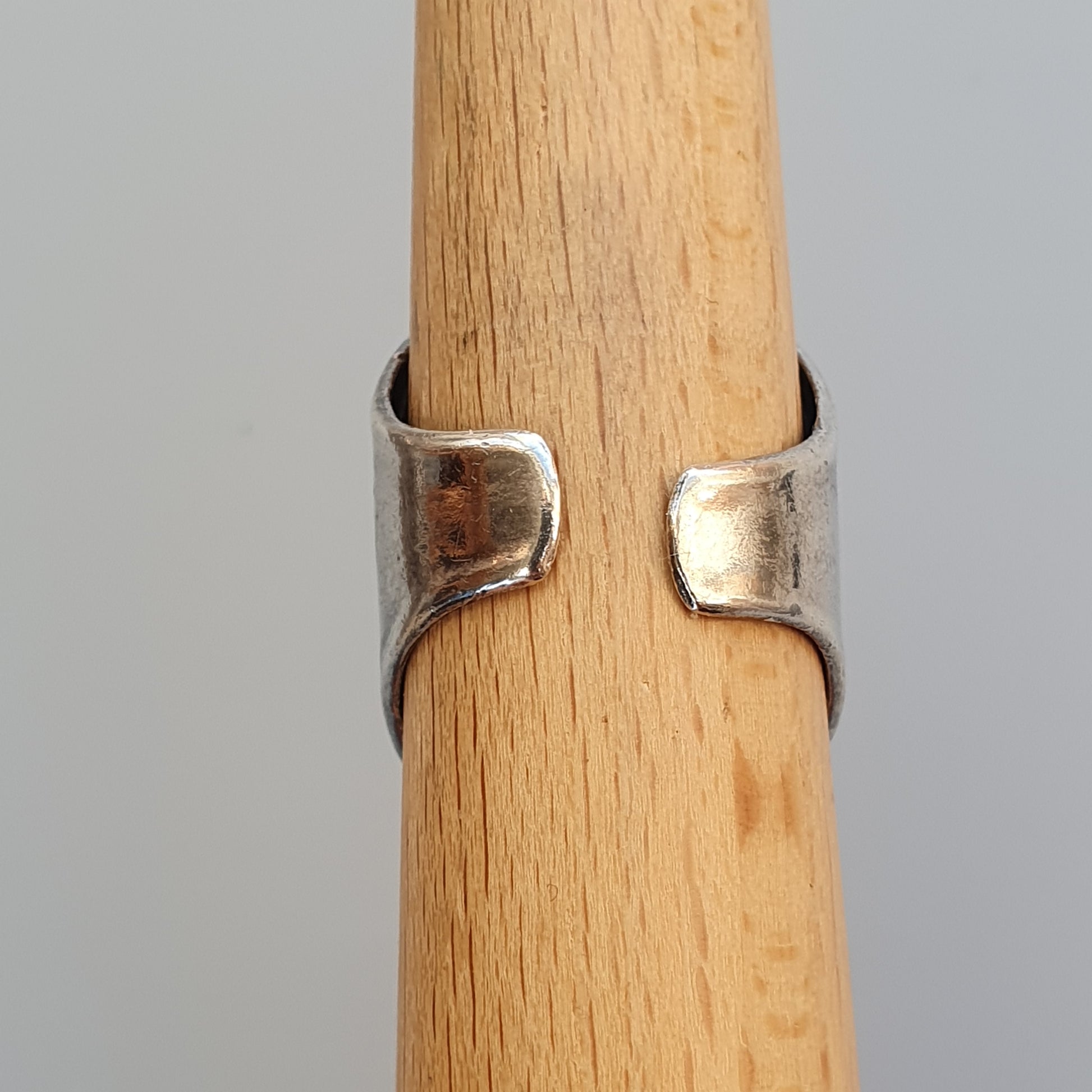 Silver ring with an open design wrapped around a wooden cylinder.