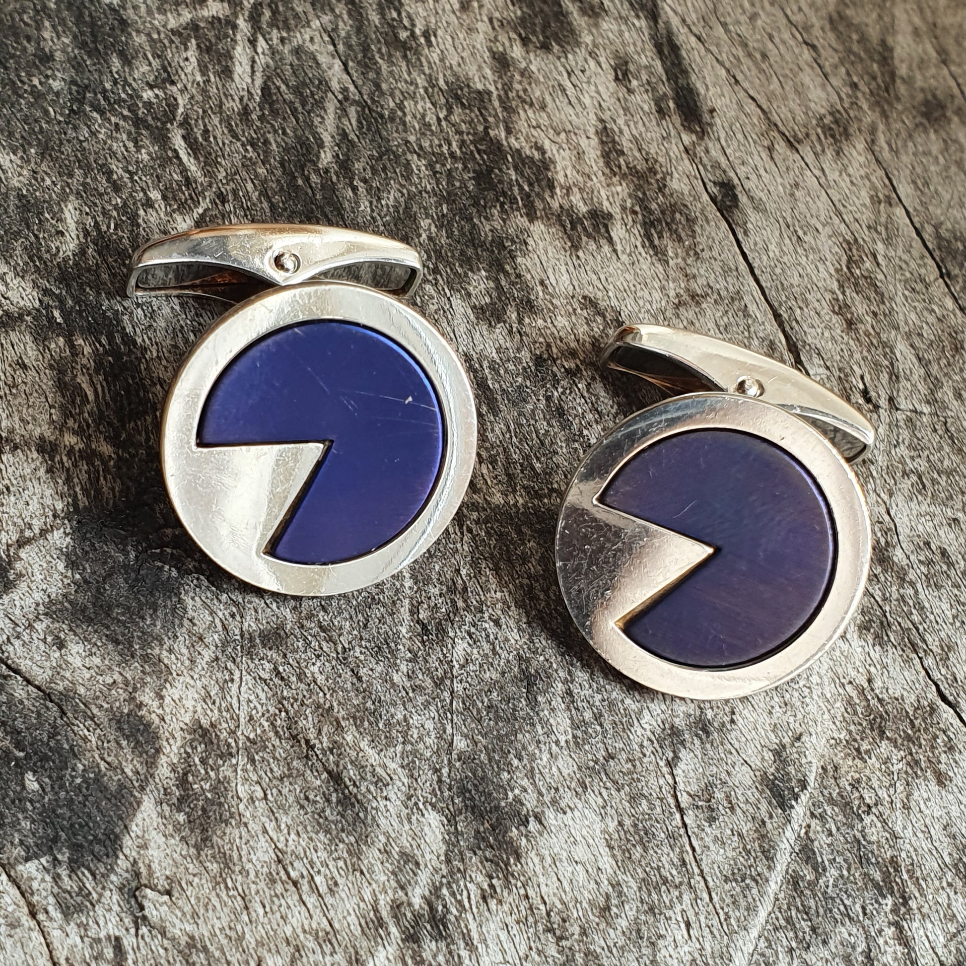 Pair of circular silver cufflinks with blue enamel inlay resembling Pac-Man shapes.