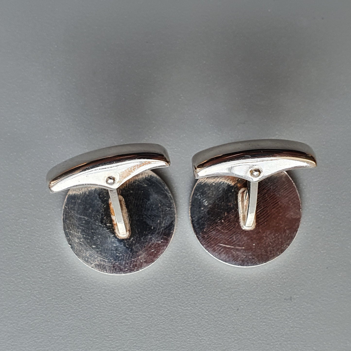 Pair of round silver cufflinks with T-shaped bars.