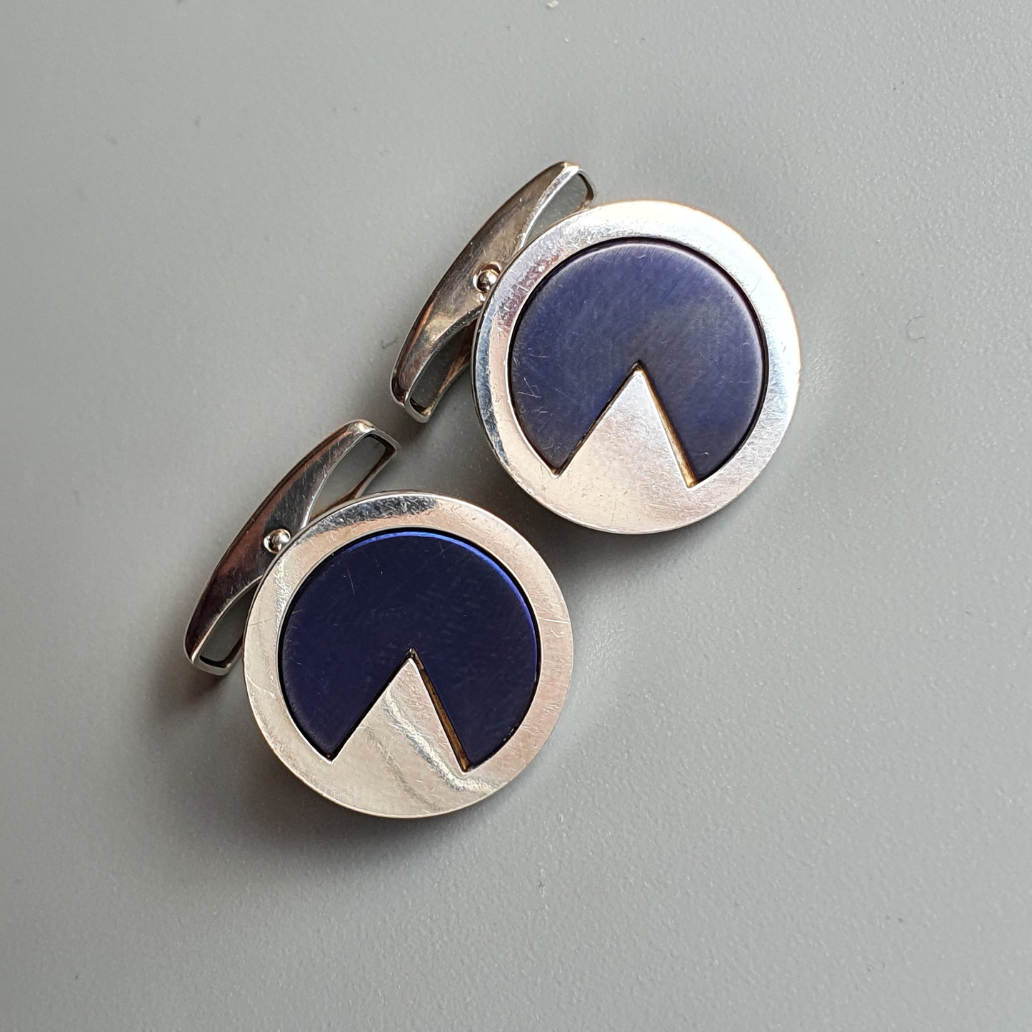 Pair of circular silver cufflinks with blue and white geometric design.