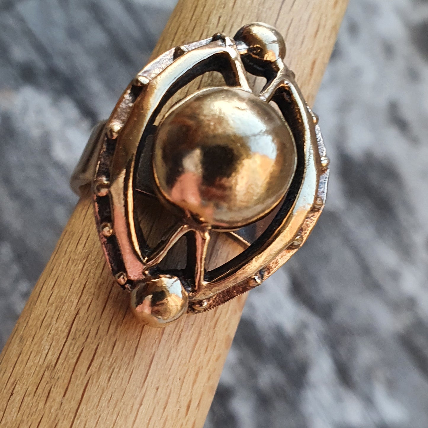 Ornate gold-toned ring featuring a spherical centerpiece within an intricate oval design.