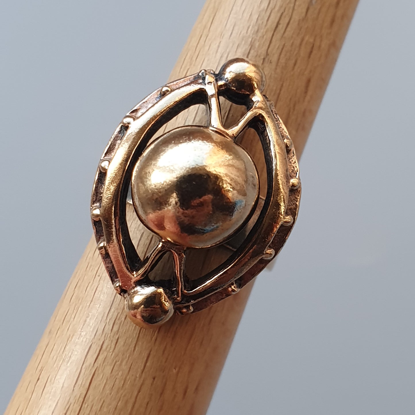 Gold-toned ring with an oval design featuring a central sphere surrounded by decorative metalwork.