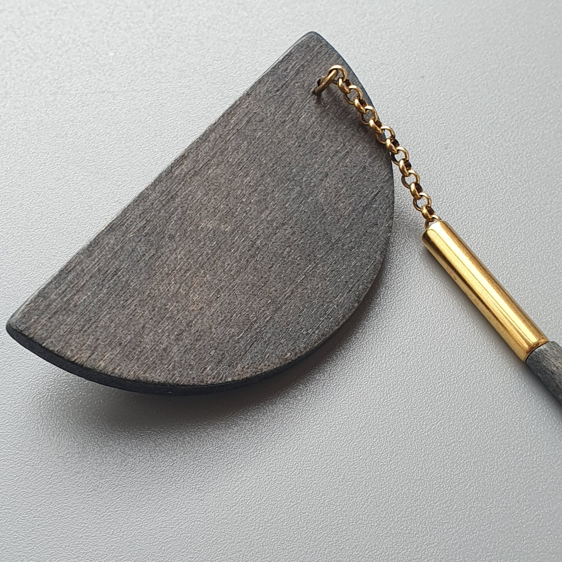 Half-moon shaped stone or wooden object with a gold-toned metal handle attached.