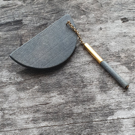 Semi-circular black wooden tool with a gold and gray handle attached by a chain.