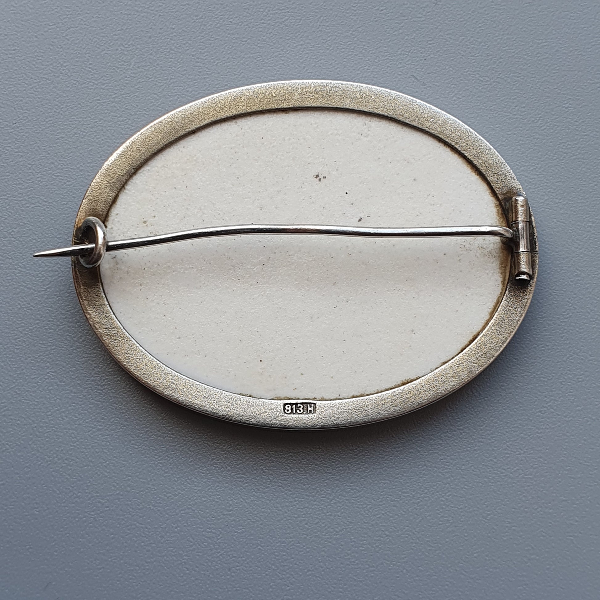 Oval-shaped ceramic brooch with a metal pin across its center.