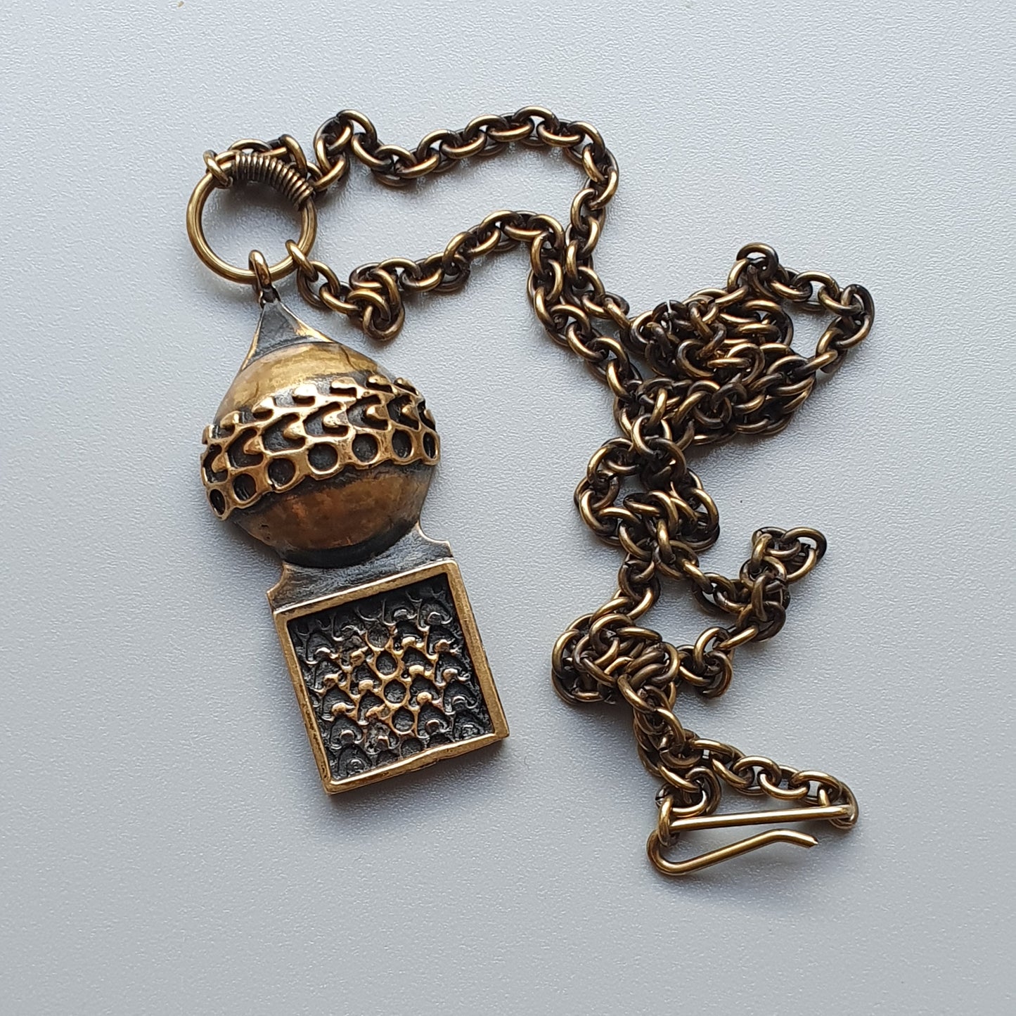 Antique-style brass necklace with a spherical pendant and square charm attached to a chain.