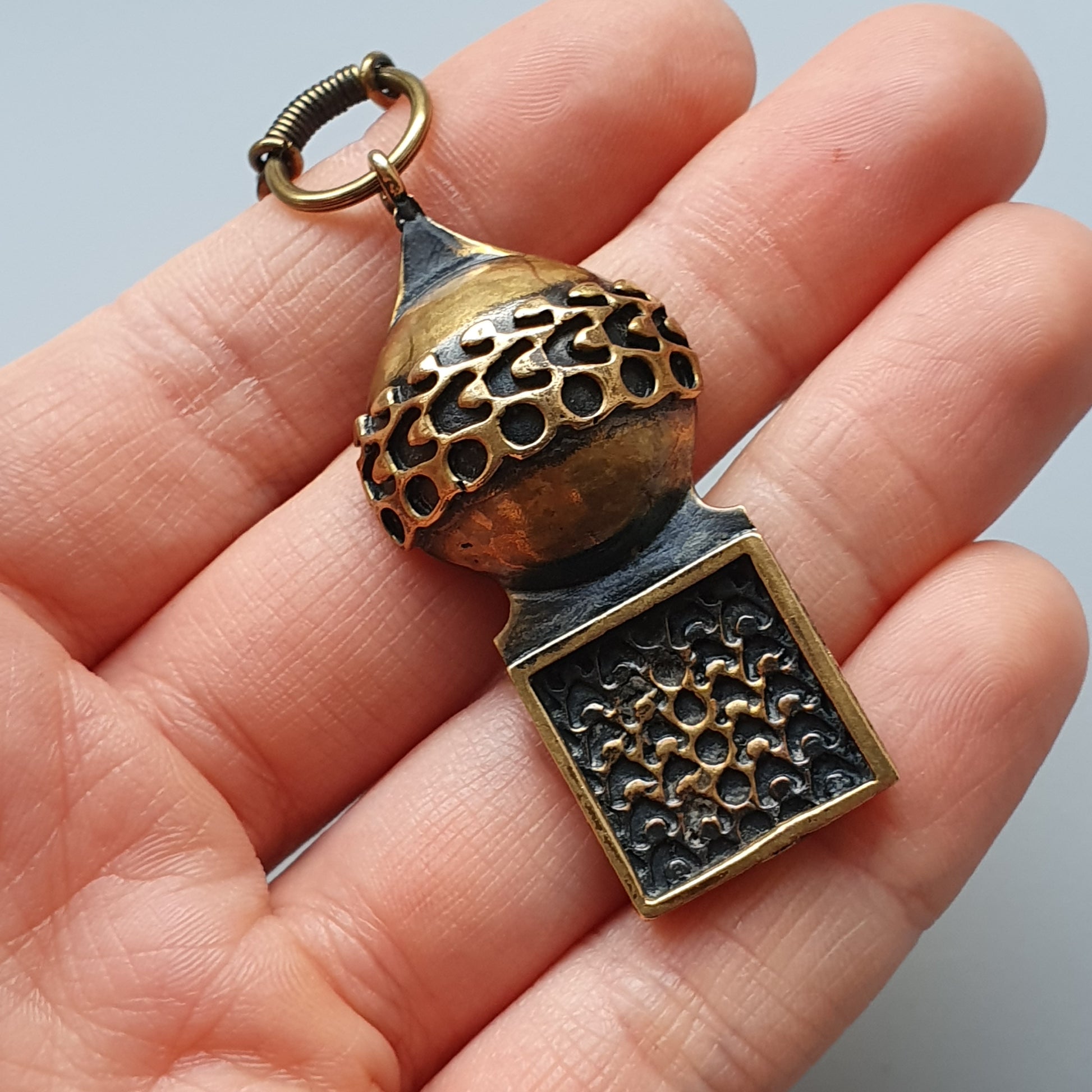 Ornate metal pendant with a spherical top and square bottom, featuring intricate cutout patterns.