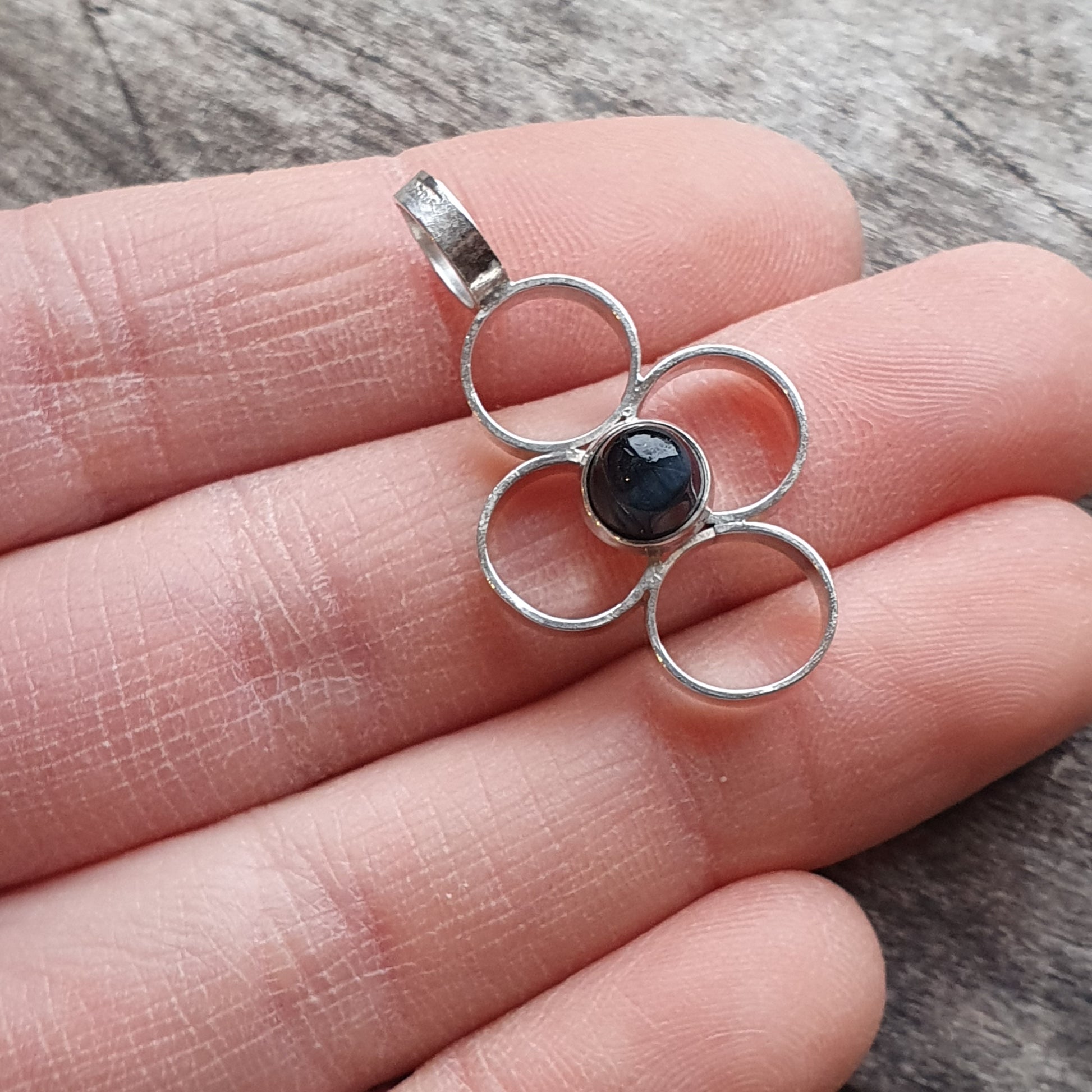 Silver pendant with a flower-like design featuring a dark blue stone in the center.