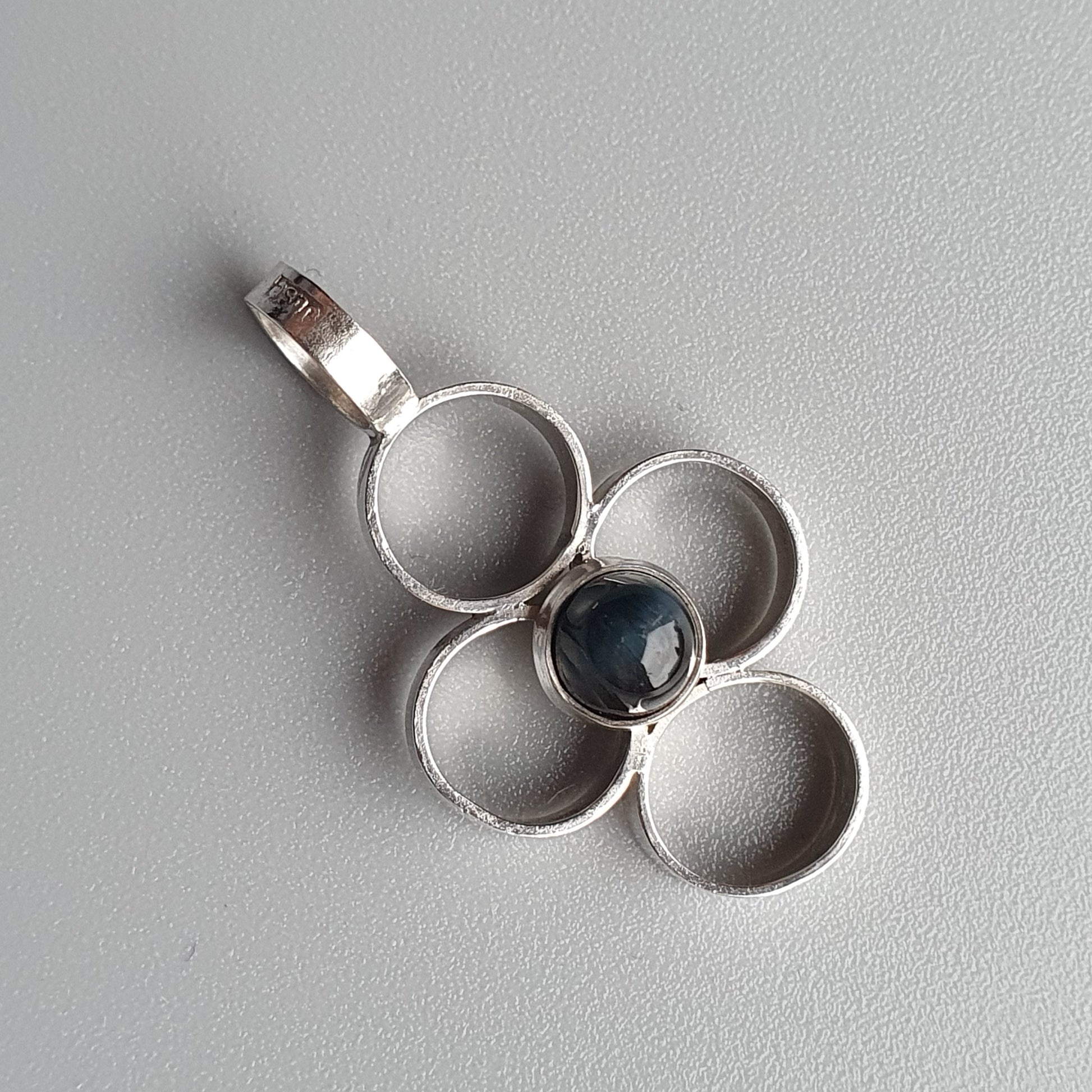 Silver pendant with a four-petal flower design and a dark blue gemstone center.