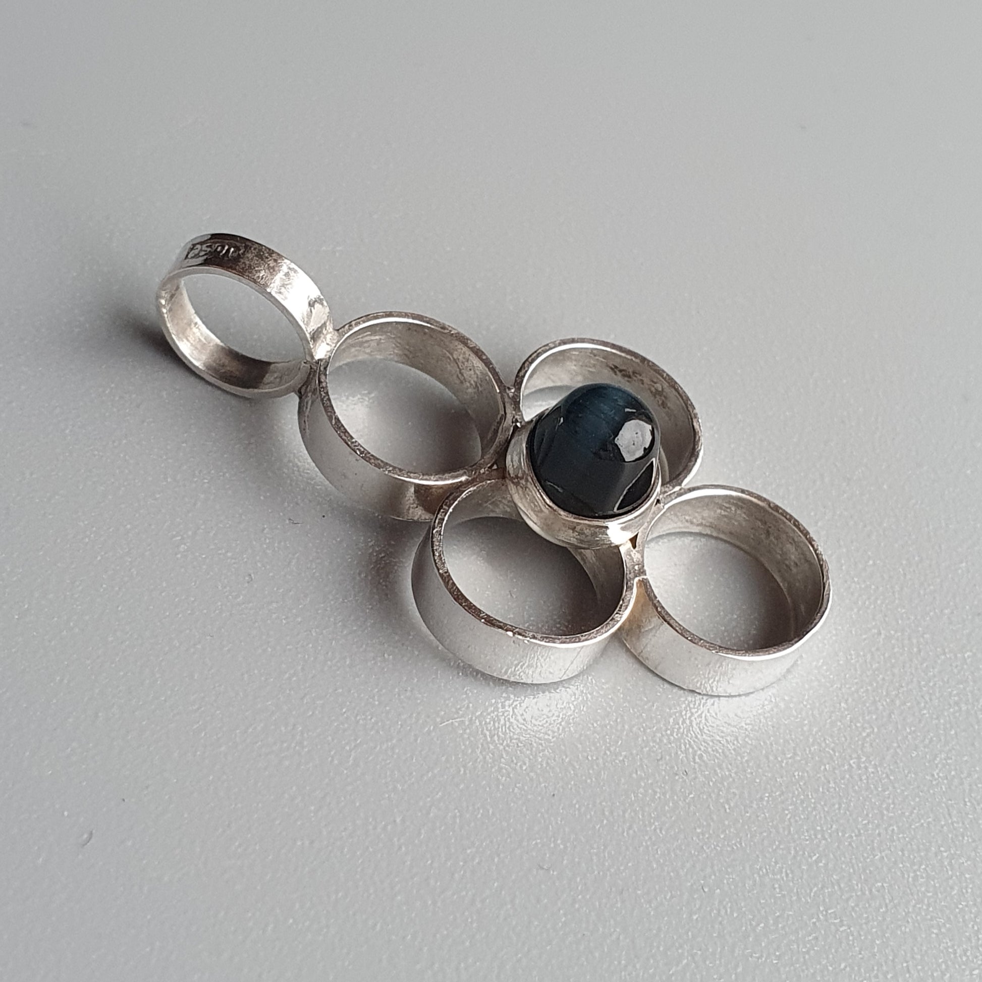 Silver pendant with interconnected rings and a dark blue gemstone.