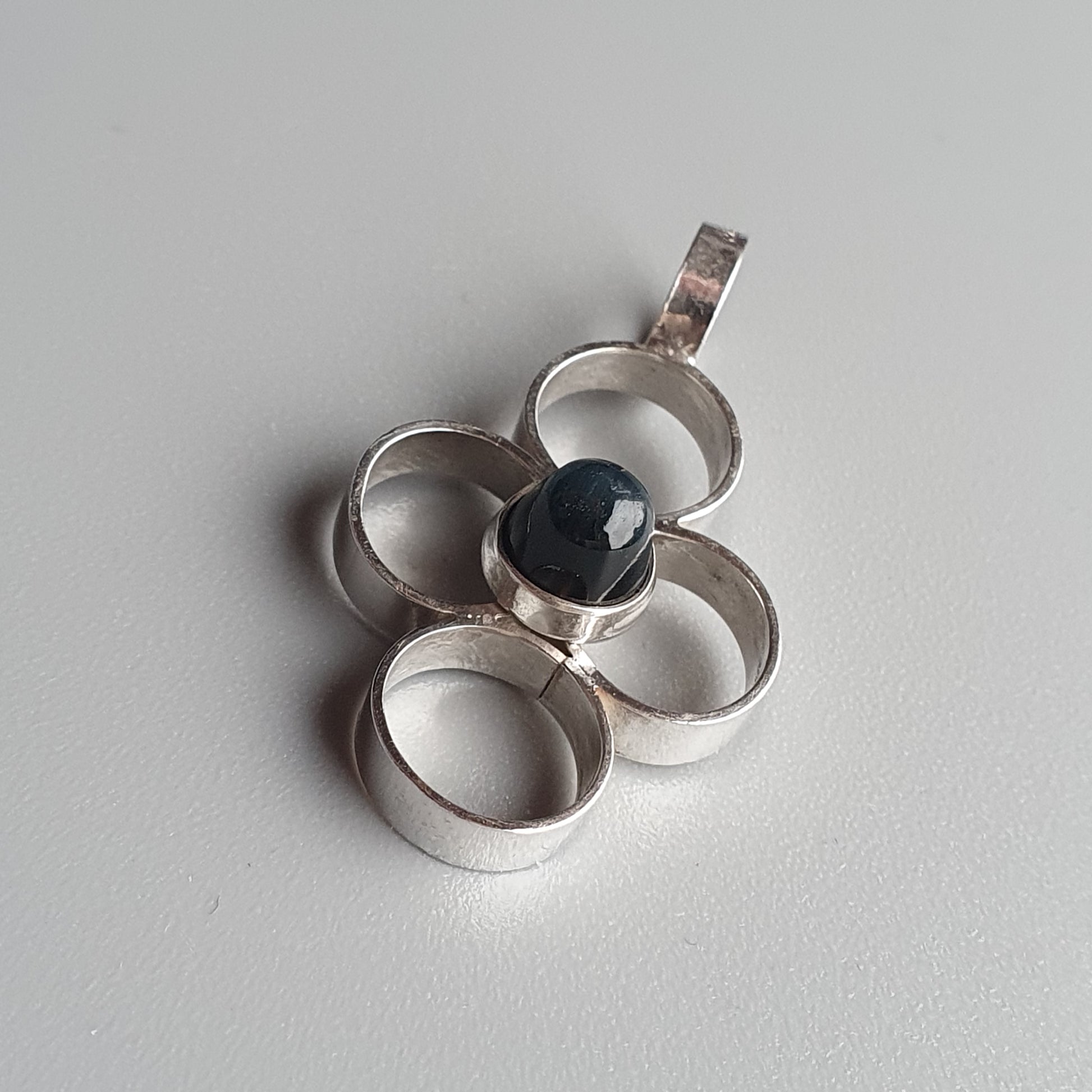 Silver pendant featuring a flower-like design with a dark blue stone in the center.