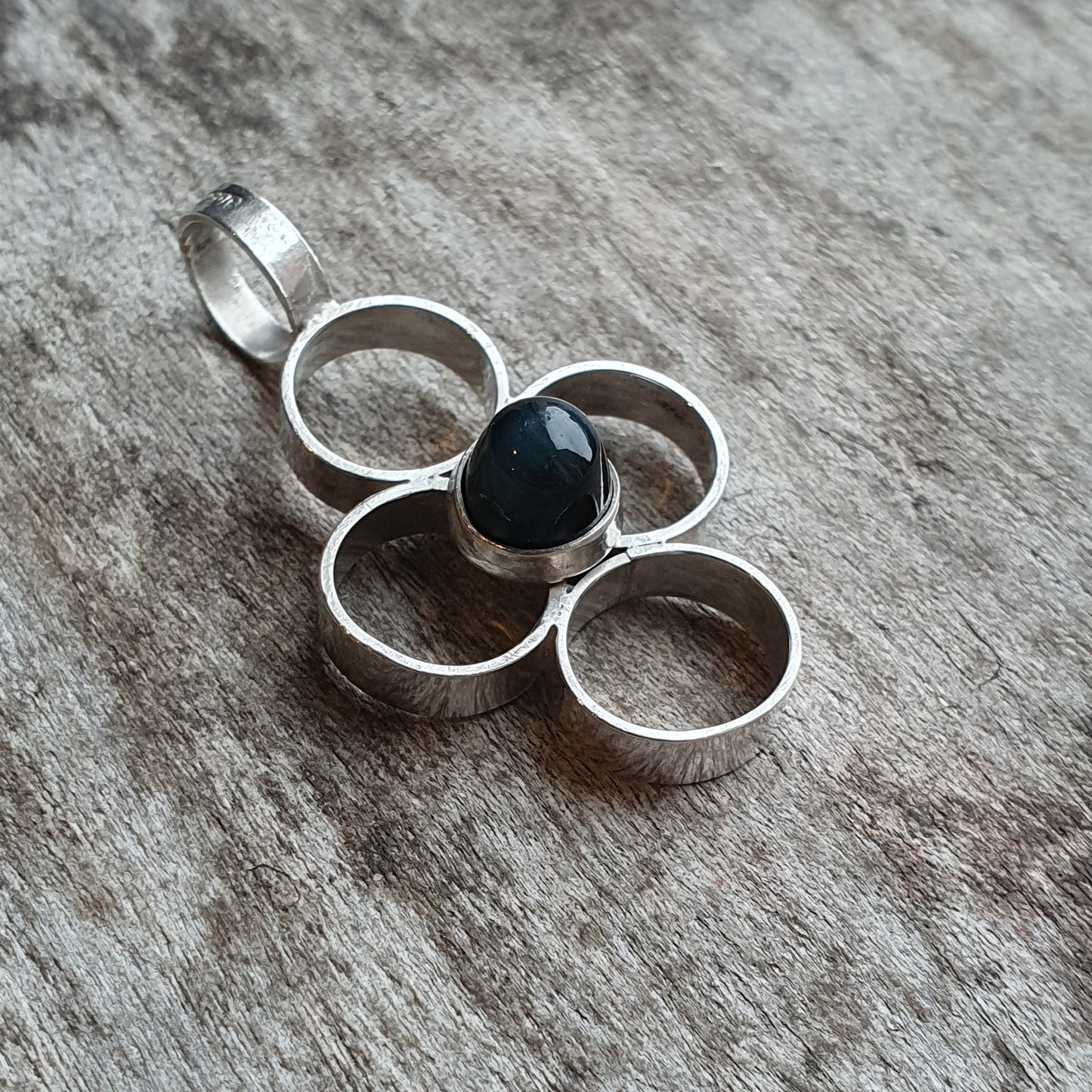 Silver pendant with four interconnected rings and a central black stone.