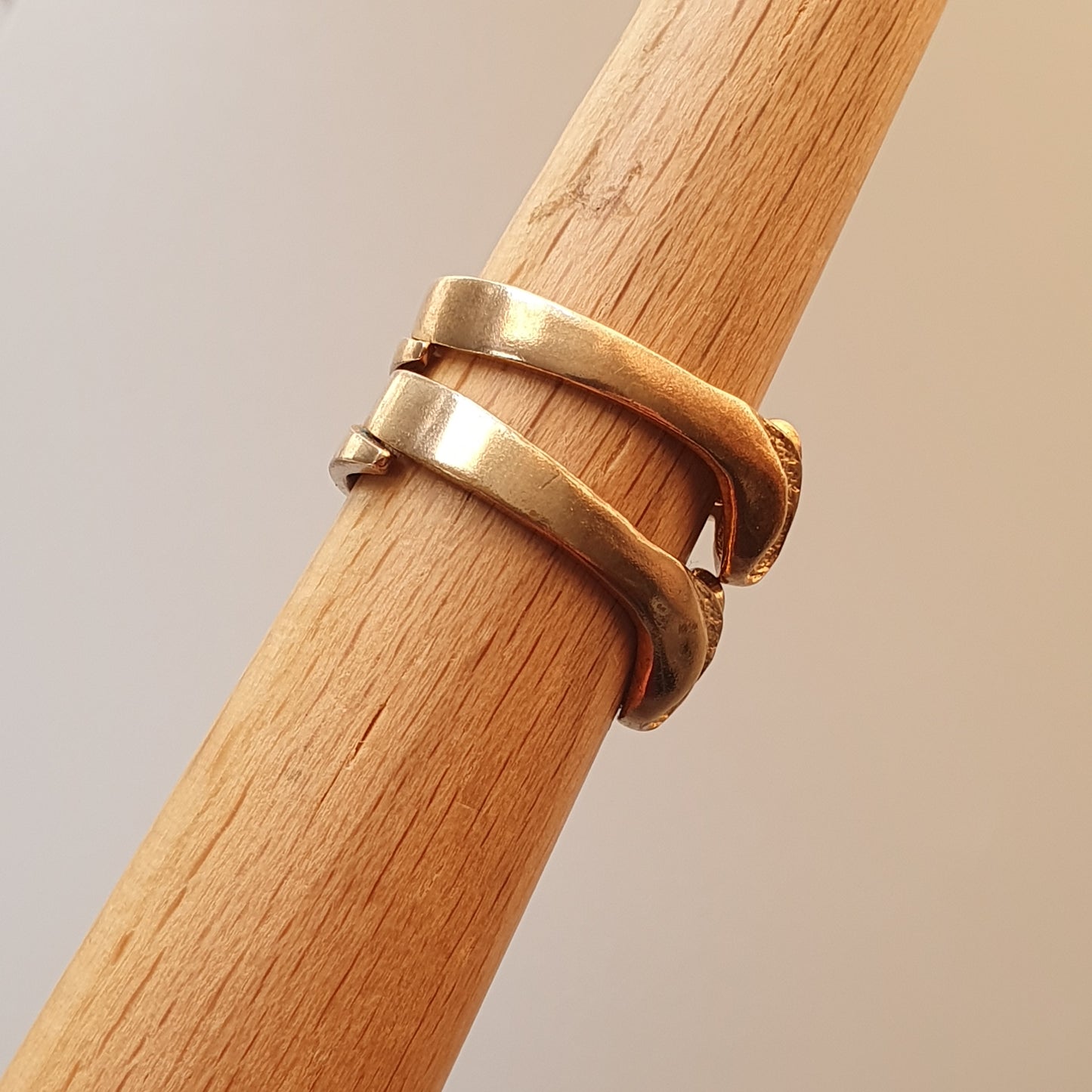 Gold ring with a unique overlapping design wrapped around a wooden dowel.