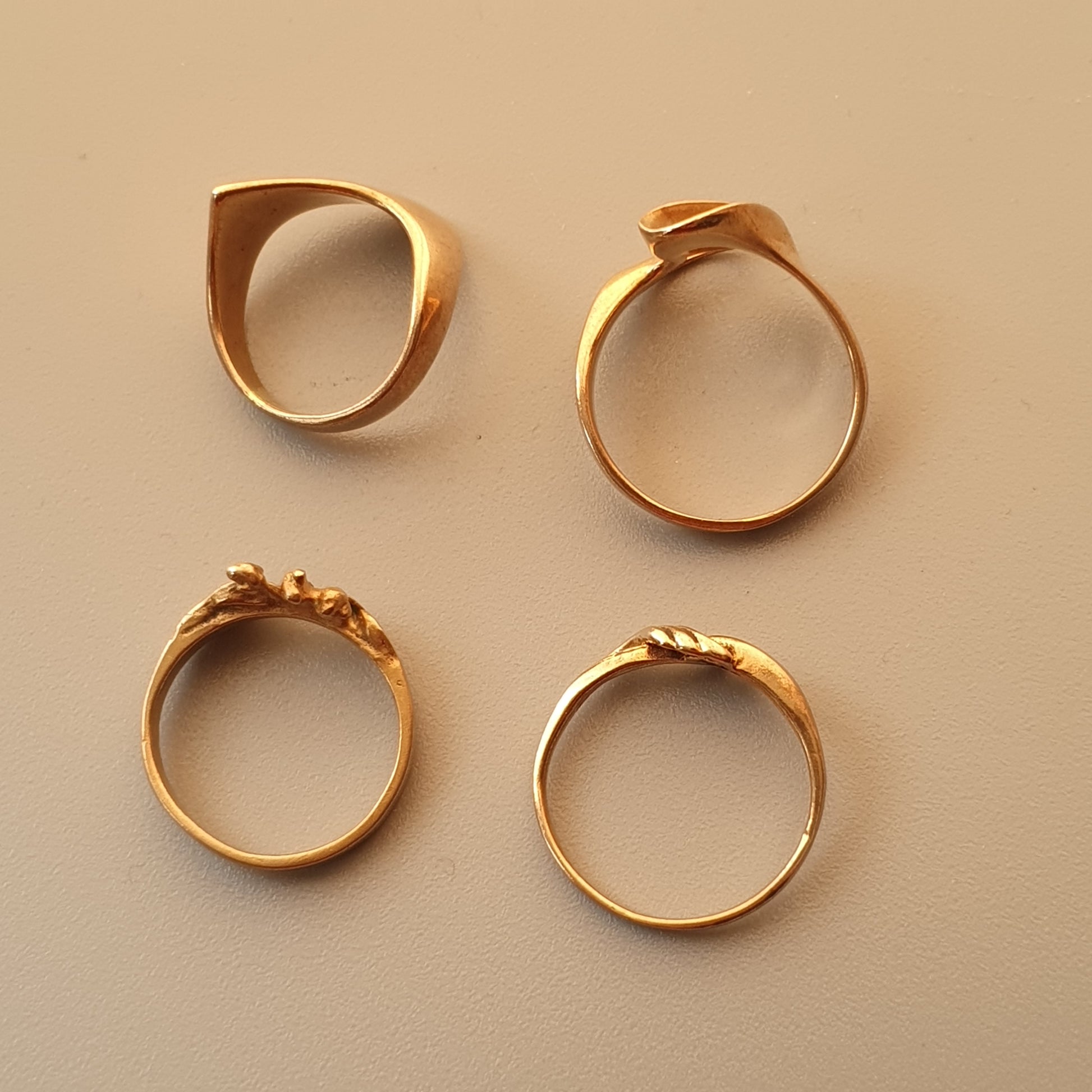 Four gold rings with different designs displayed on a neutral background.