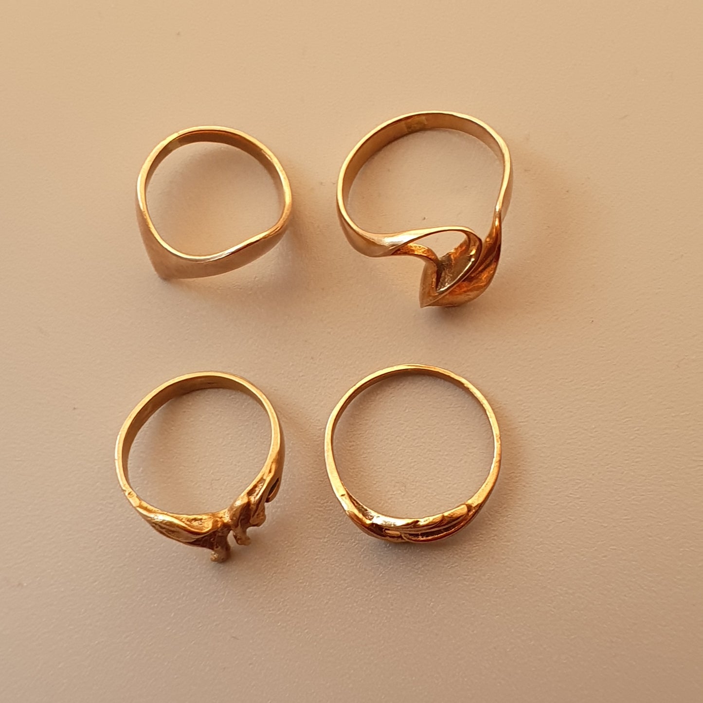 Four gold rings with varying designs displayed on a neutral background.