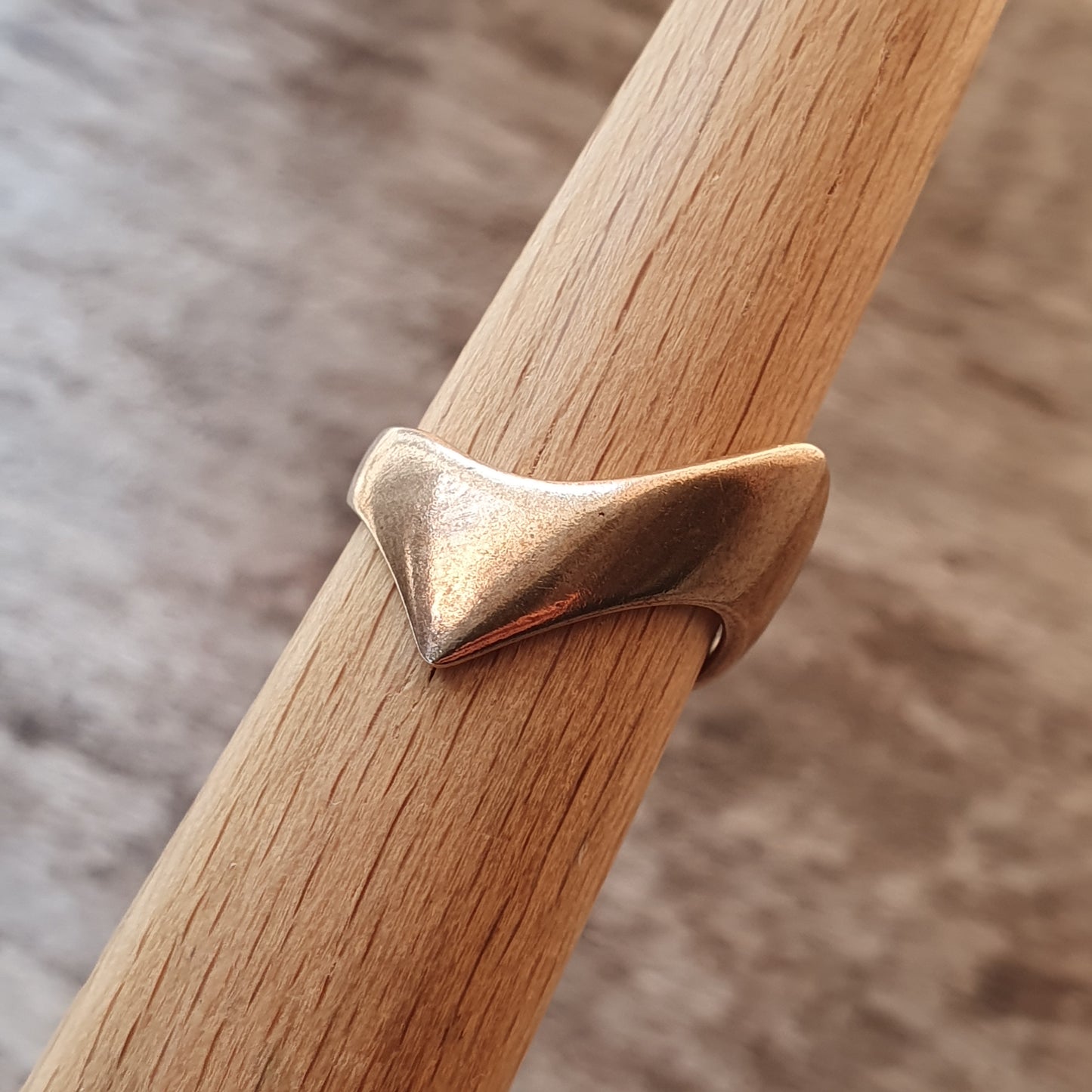 Gold-colored ring with a unique twisted or folded design wrapped around a wooden dowel.