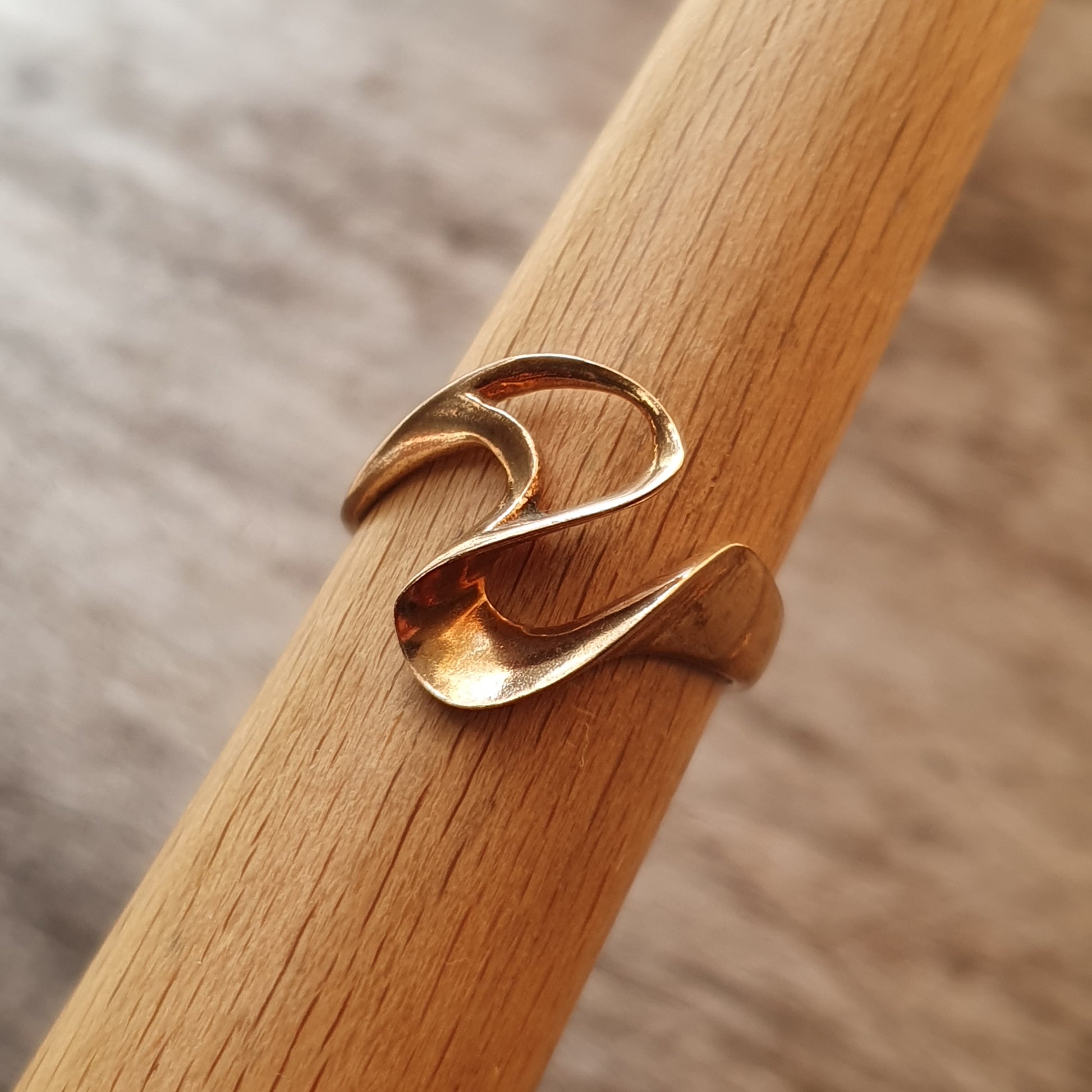 Gold ring with a wave-like design wrapped around a wooden dowel.