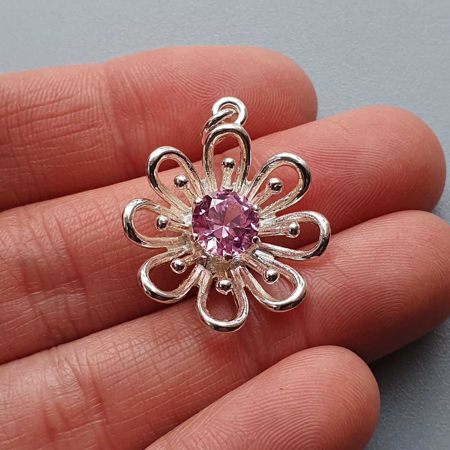 Silver flower-shaped pendant with a pink gemstone center.