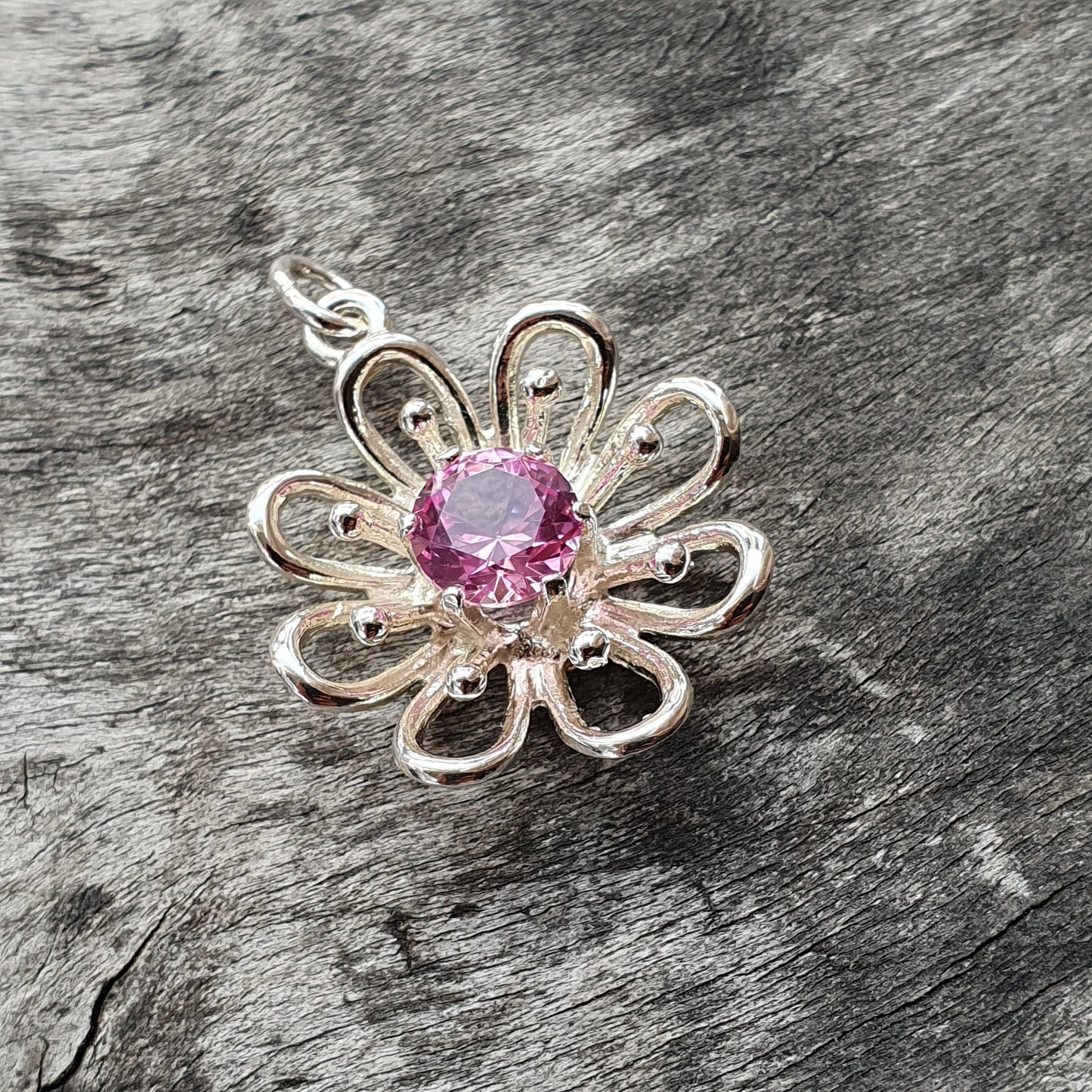 Silver flower-shaped pendant with a pink gemstone center.