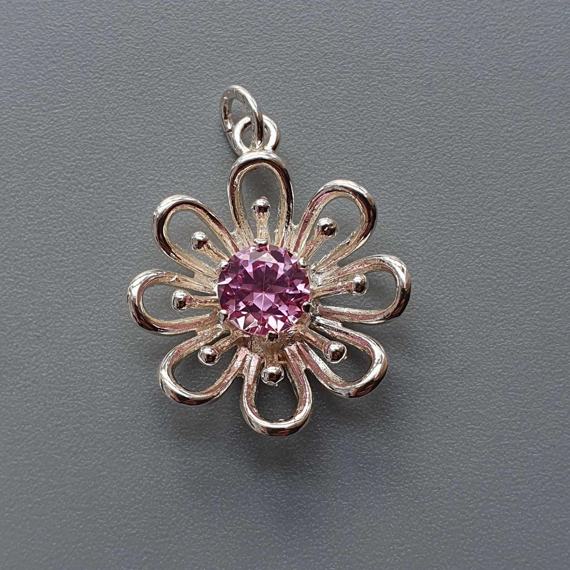 Silver flower-shaped pendant with a pink gemstone center.