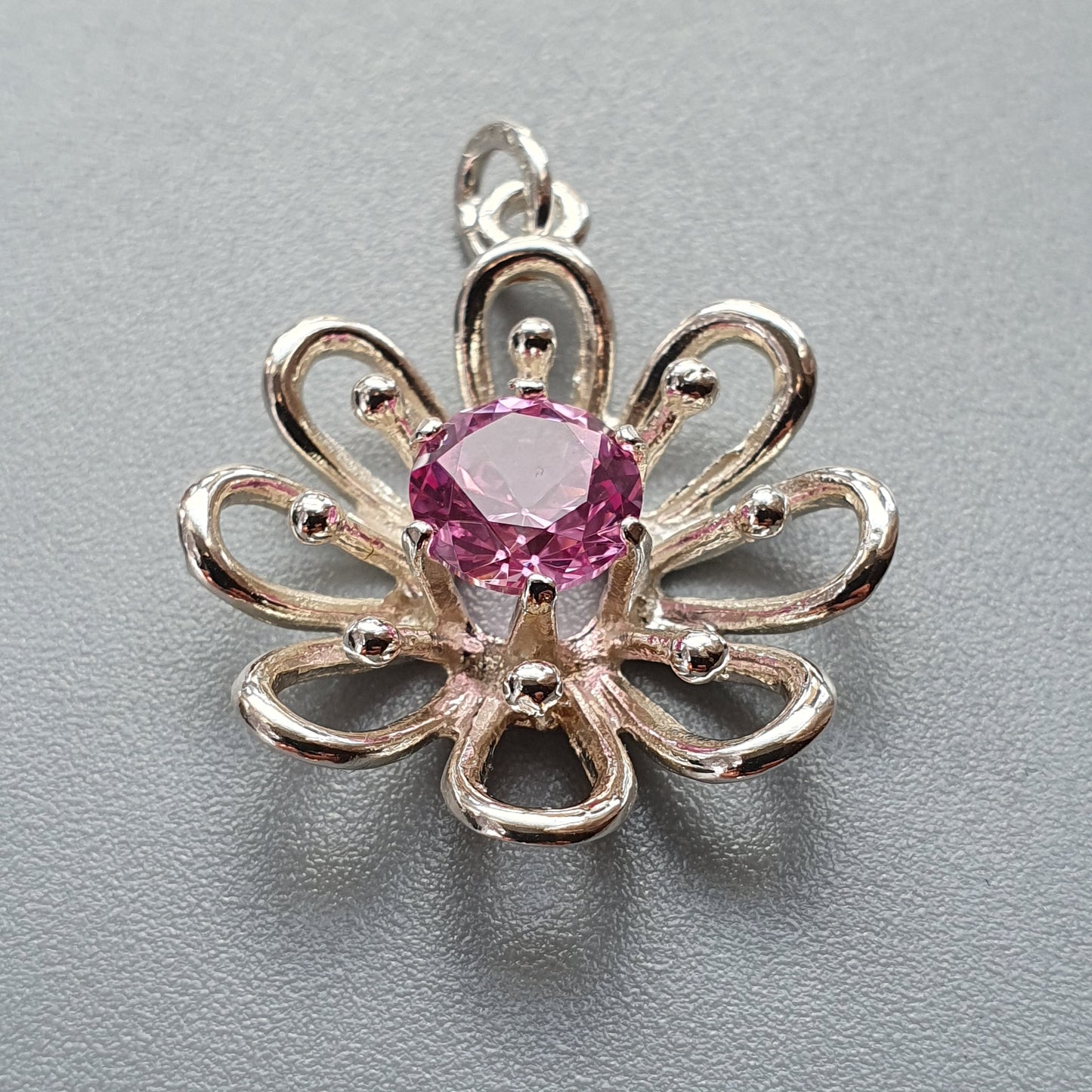 Flower-shaped silver pendant with a pink gemstone center.