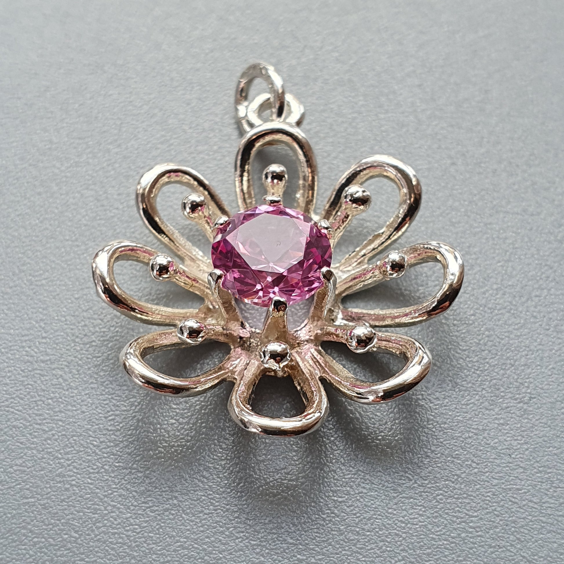 Flower-shaped silver pendant with a pink gemstone center.