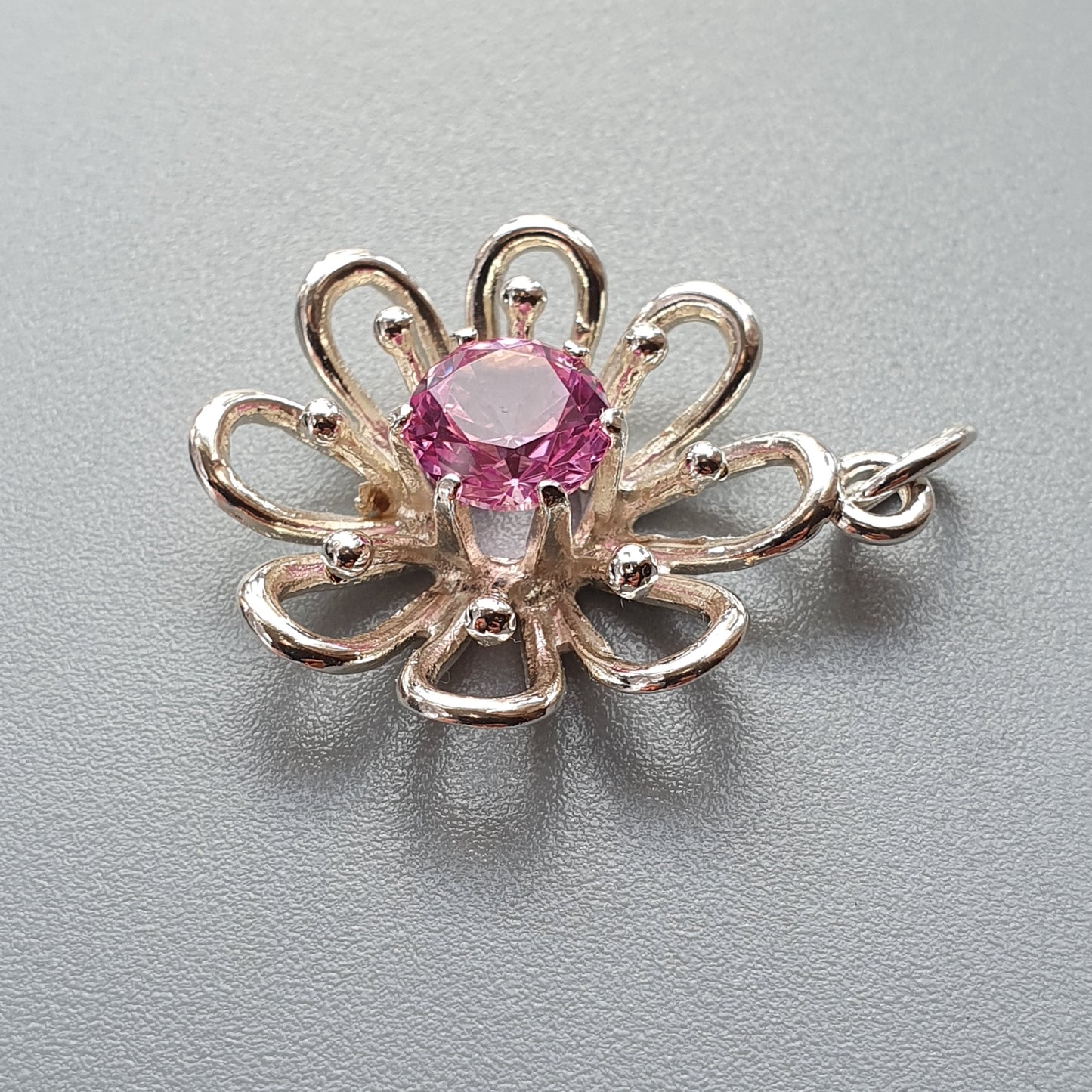 Flower-shaped pendant with a pink gemstone center and silver-toned petals.