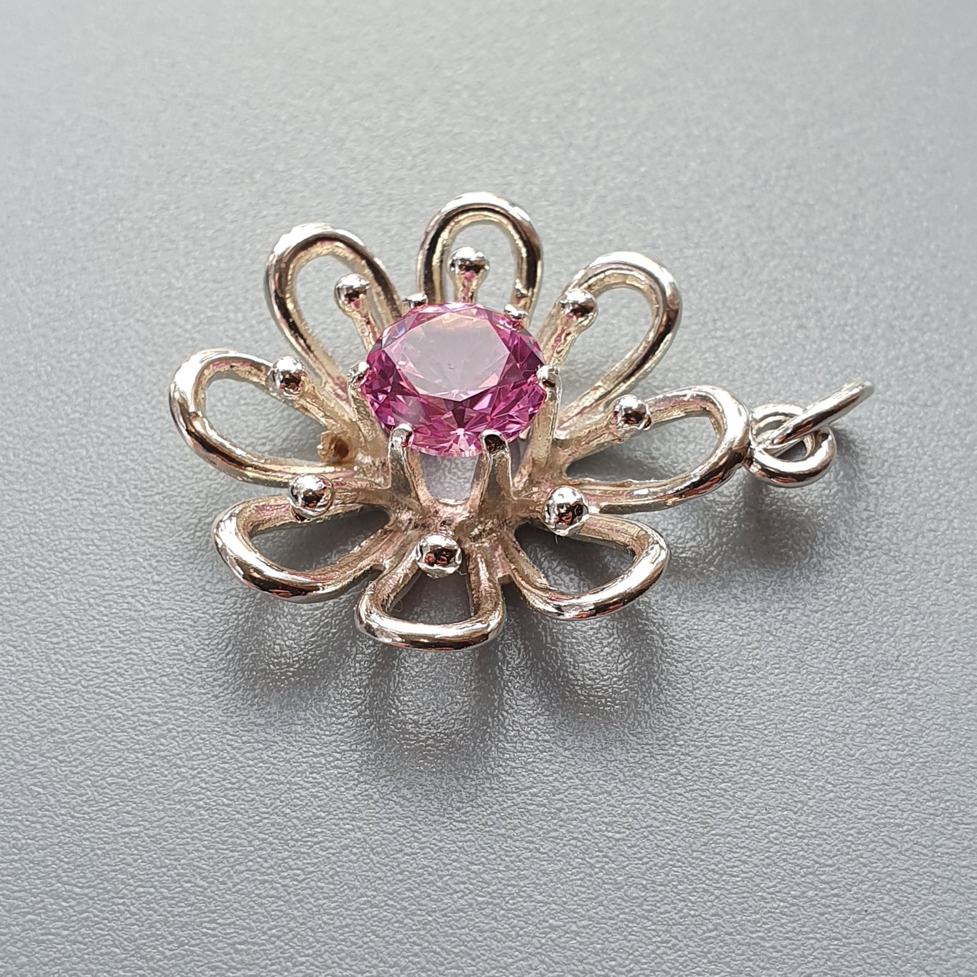 Flower-shaped pendant with a pink gemstone center and silver-toned petals.