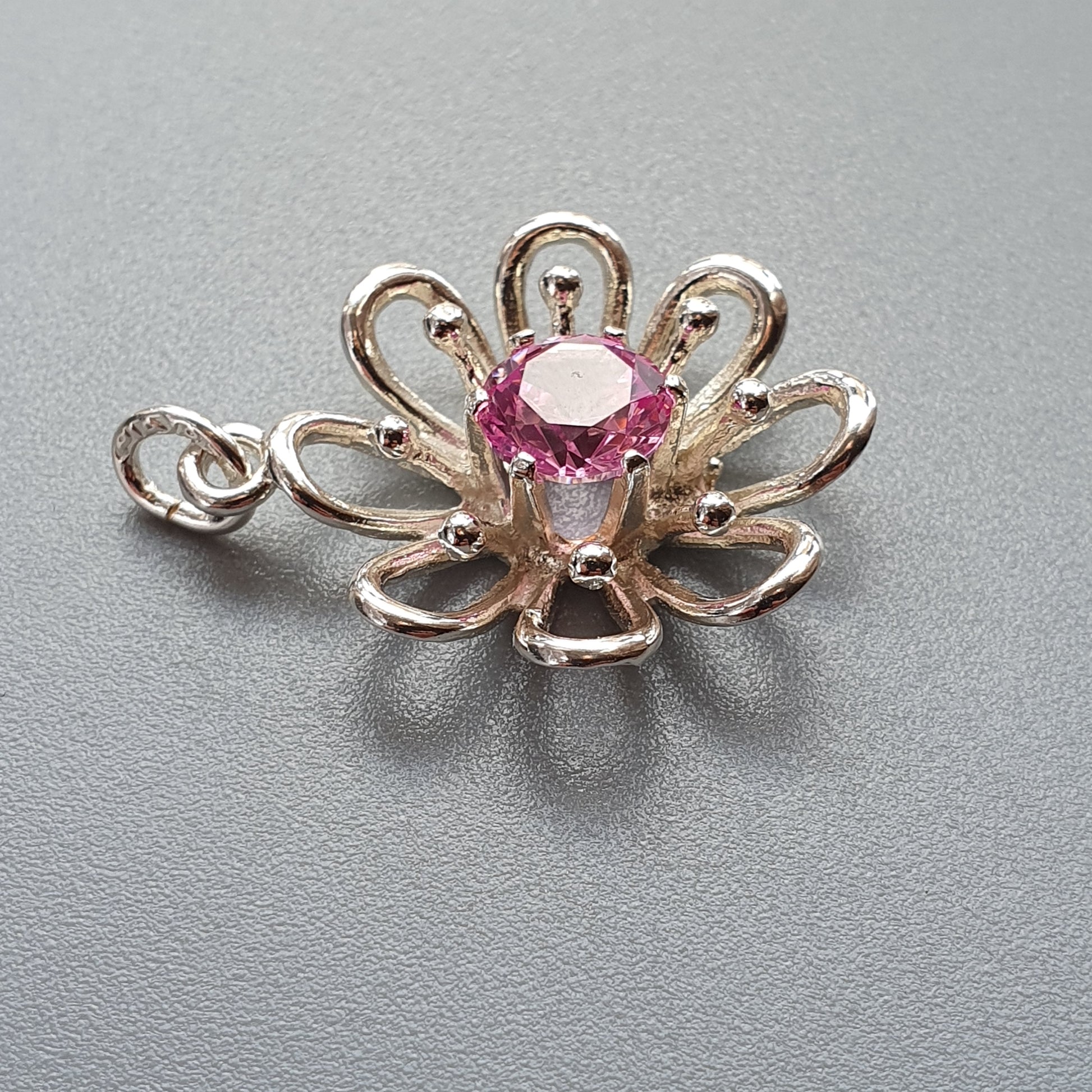 Silver flower-shaped pendant with a pink gemstone center.