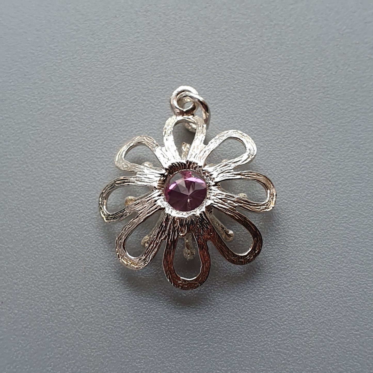 Silver flower-shaped pendant with a purple gemstone center.