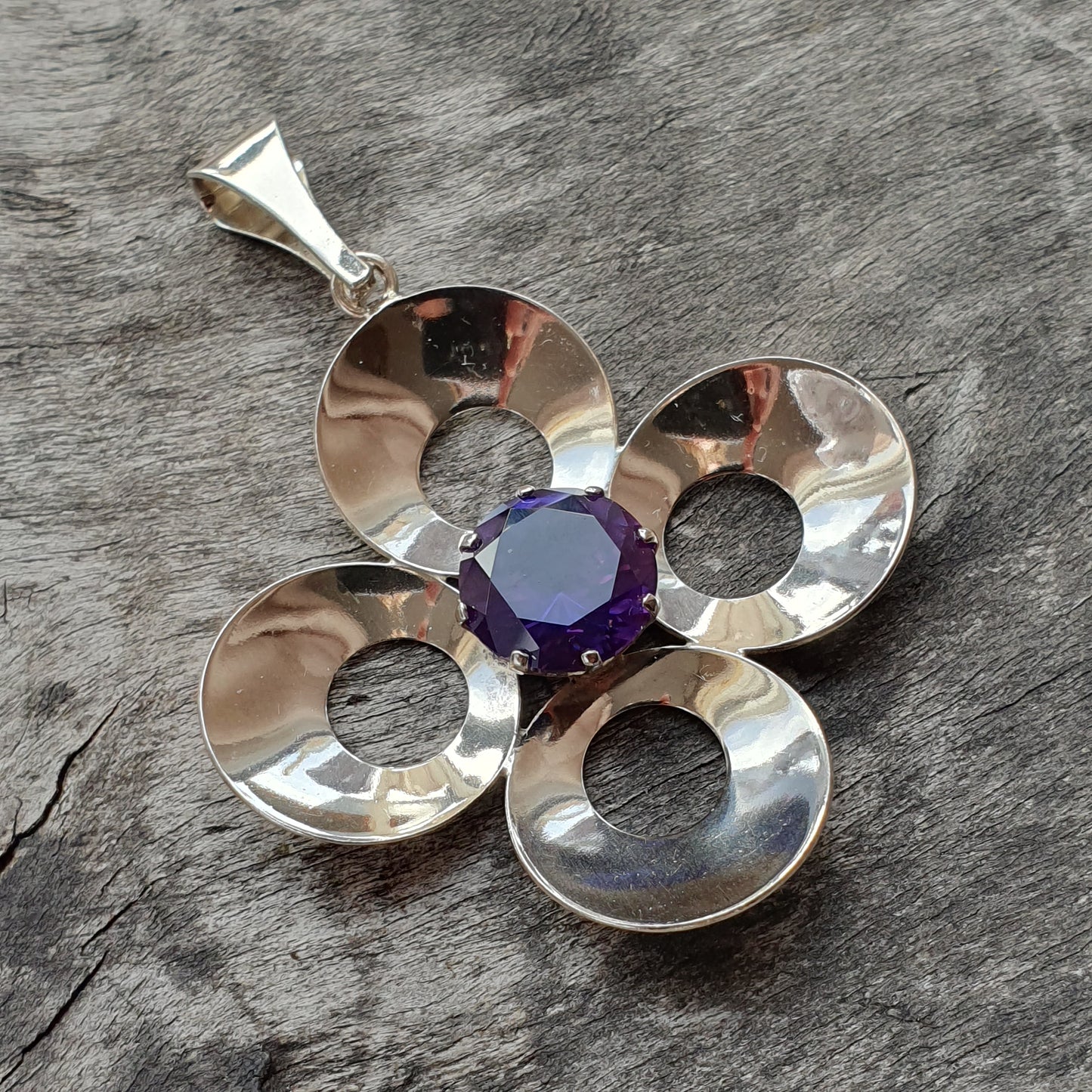 Silver flower-shaped pendant with a purple gemstone center.