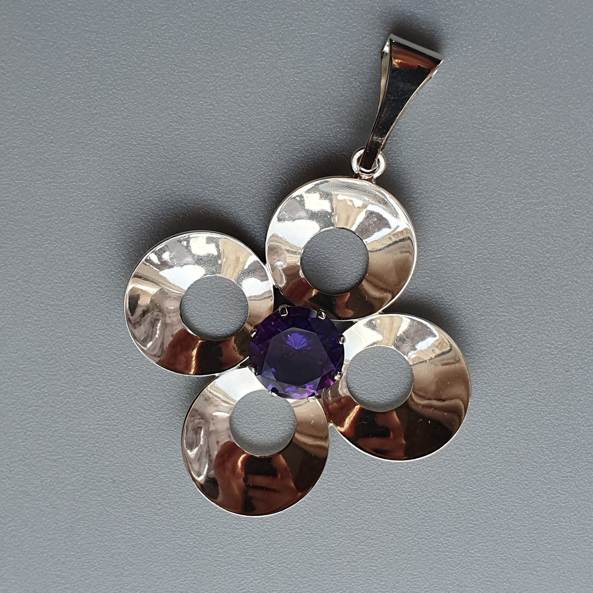 Silver flower-shaped pendant with a purple gemstone center.