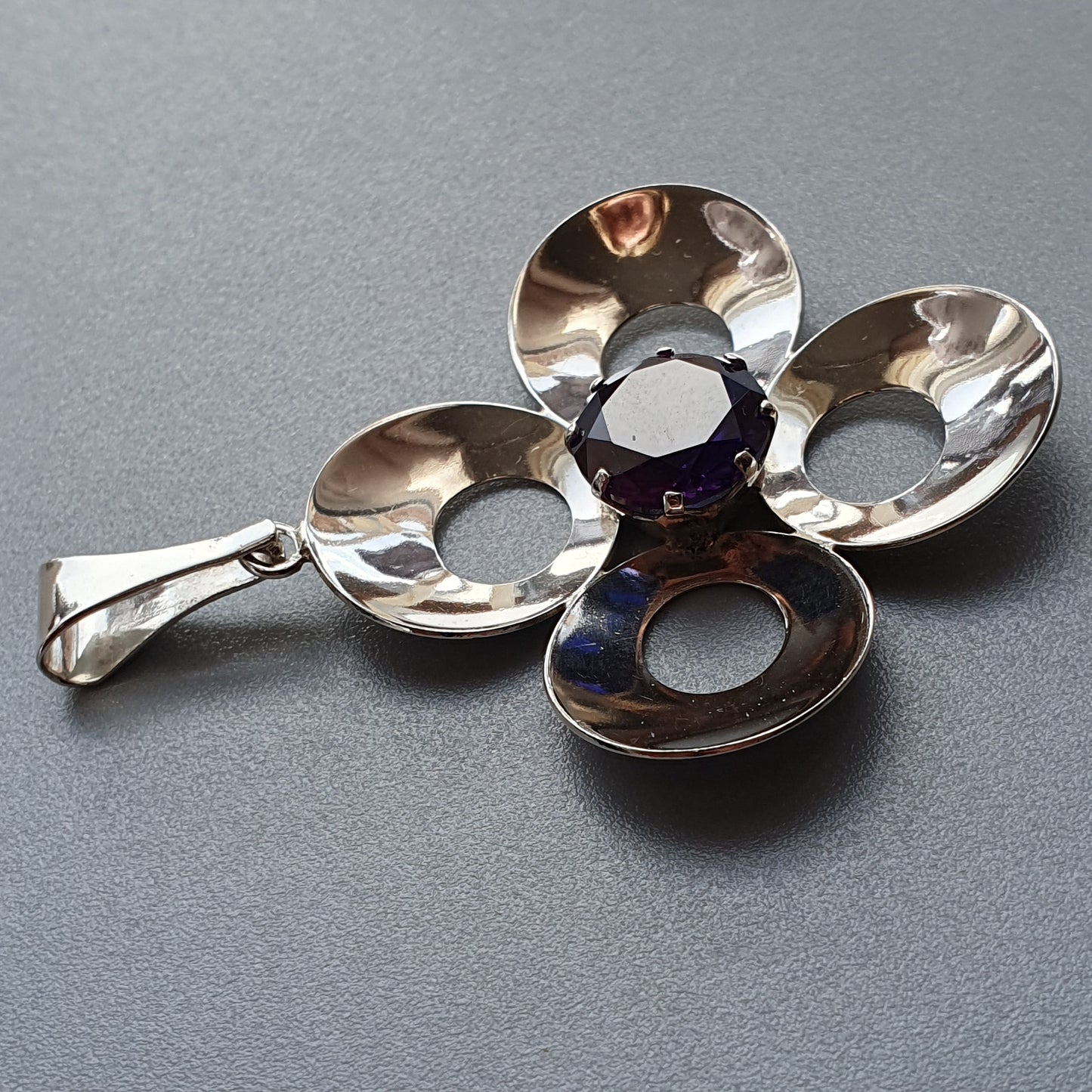 Silver pendant in the shape of a four-petaled flower with circular cutouts.