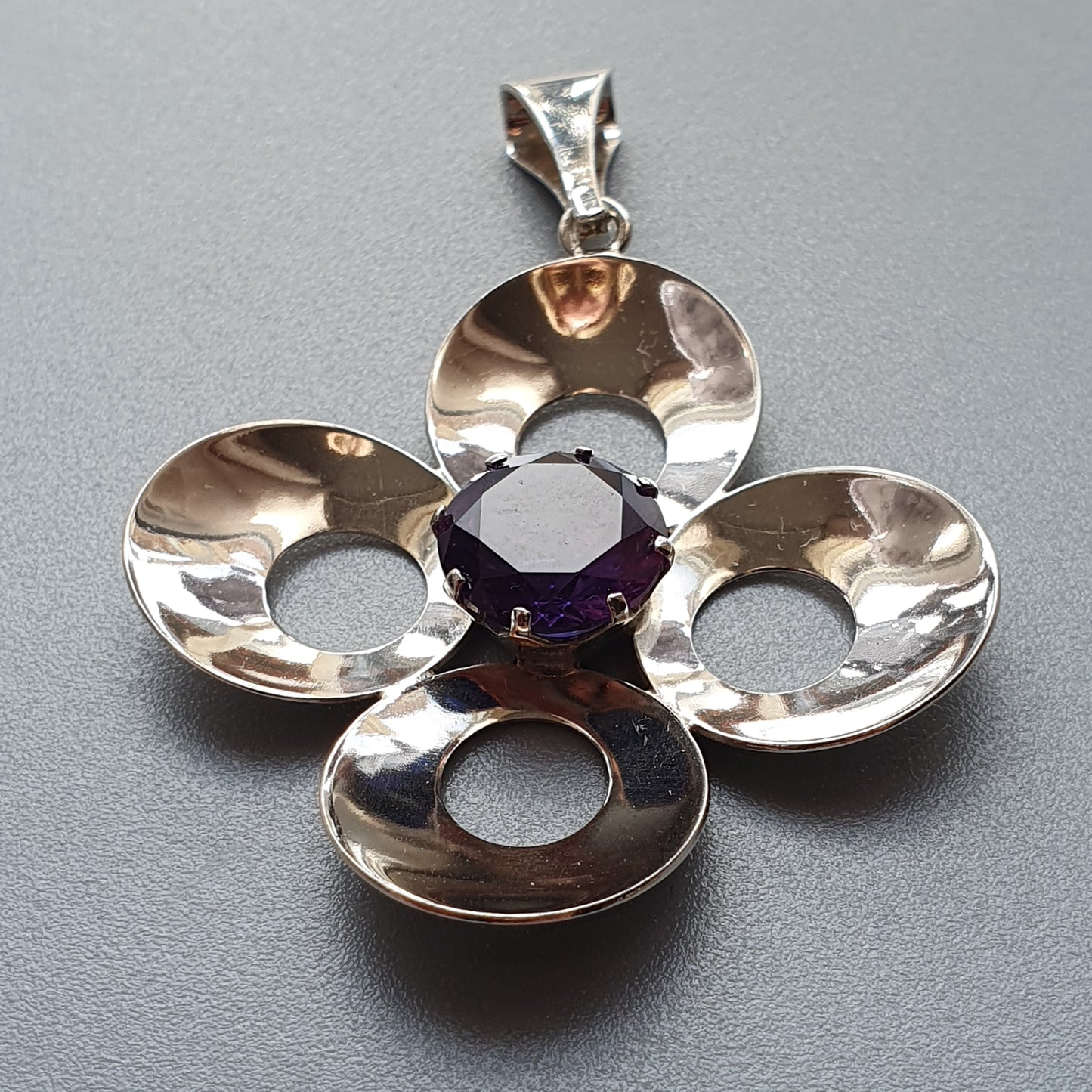 Silver pendant shaped like a four-petaled flower with a purple gemstone in the center.