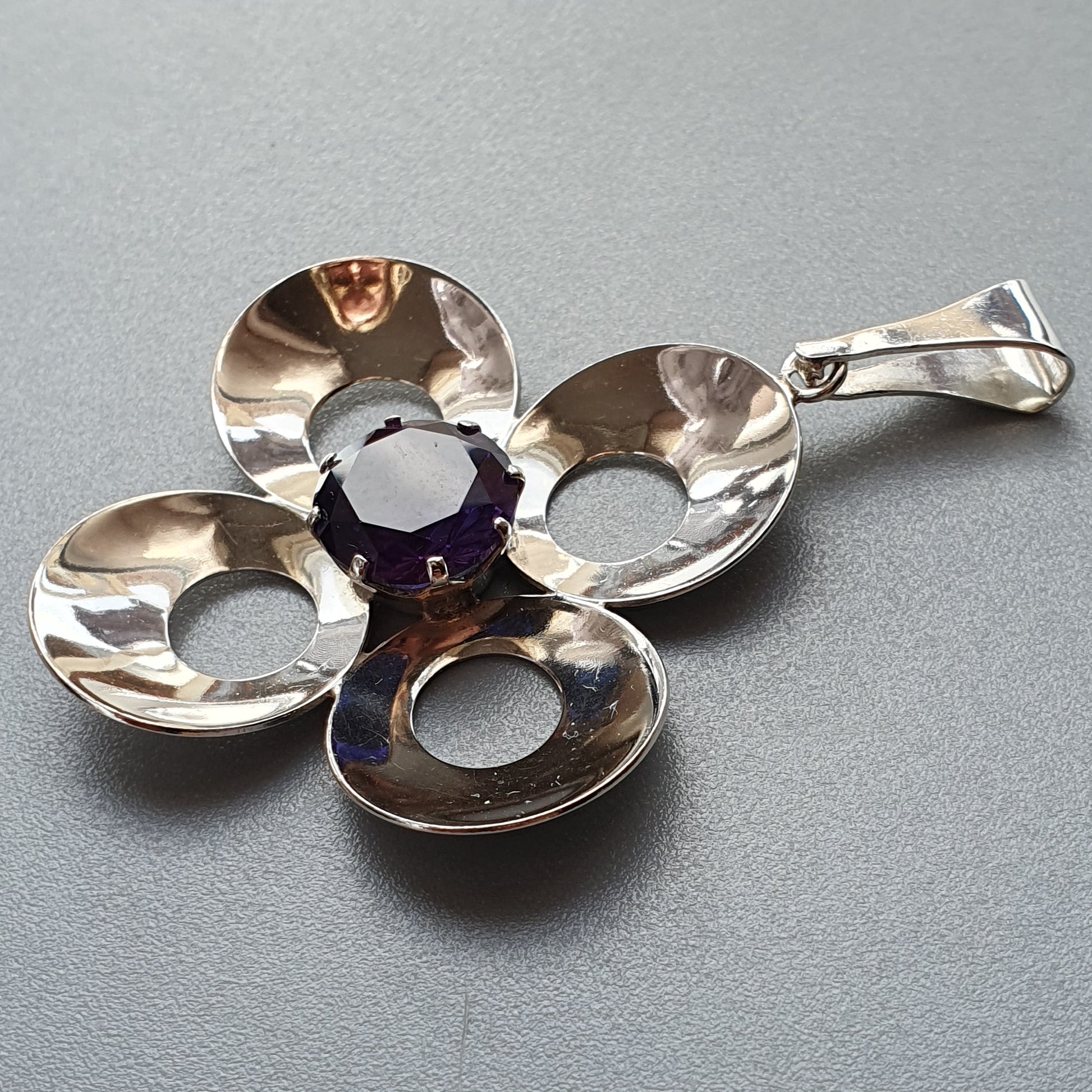 Silver pendant with a four-petal flower design and a purple gemstone center.