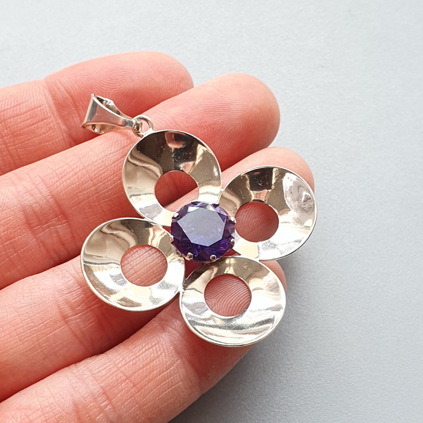 Silver flower-shaped pendant with a purple gemstone center.