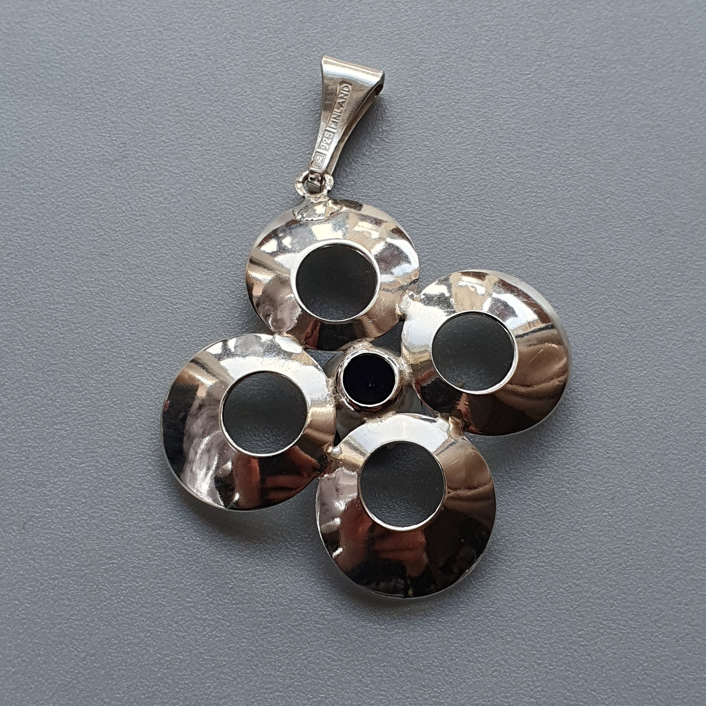 Silver pendant with circular cutouts arranged in a clover-like pattern.