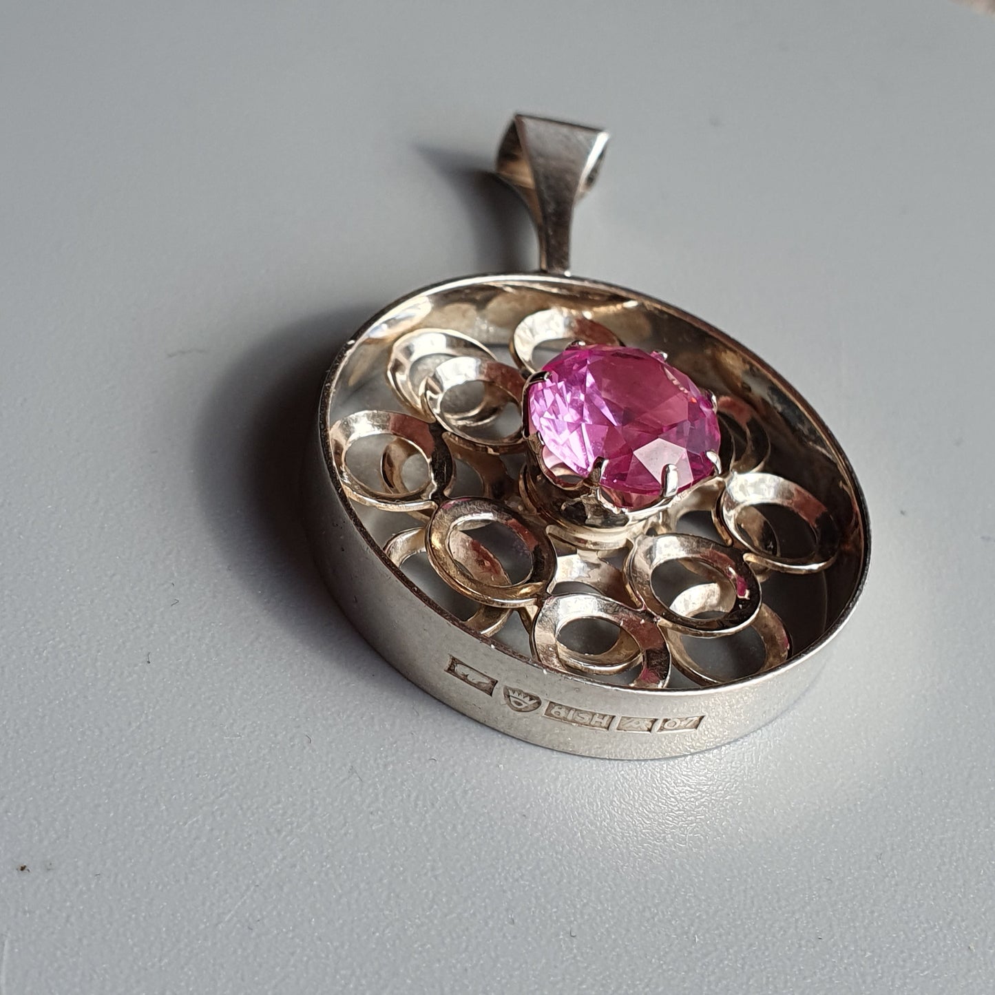 Silver pendant featuring a pink gemstone surrounded by circular cutouts.