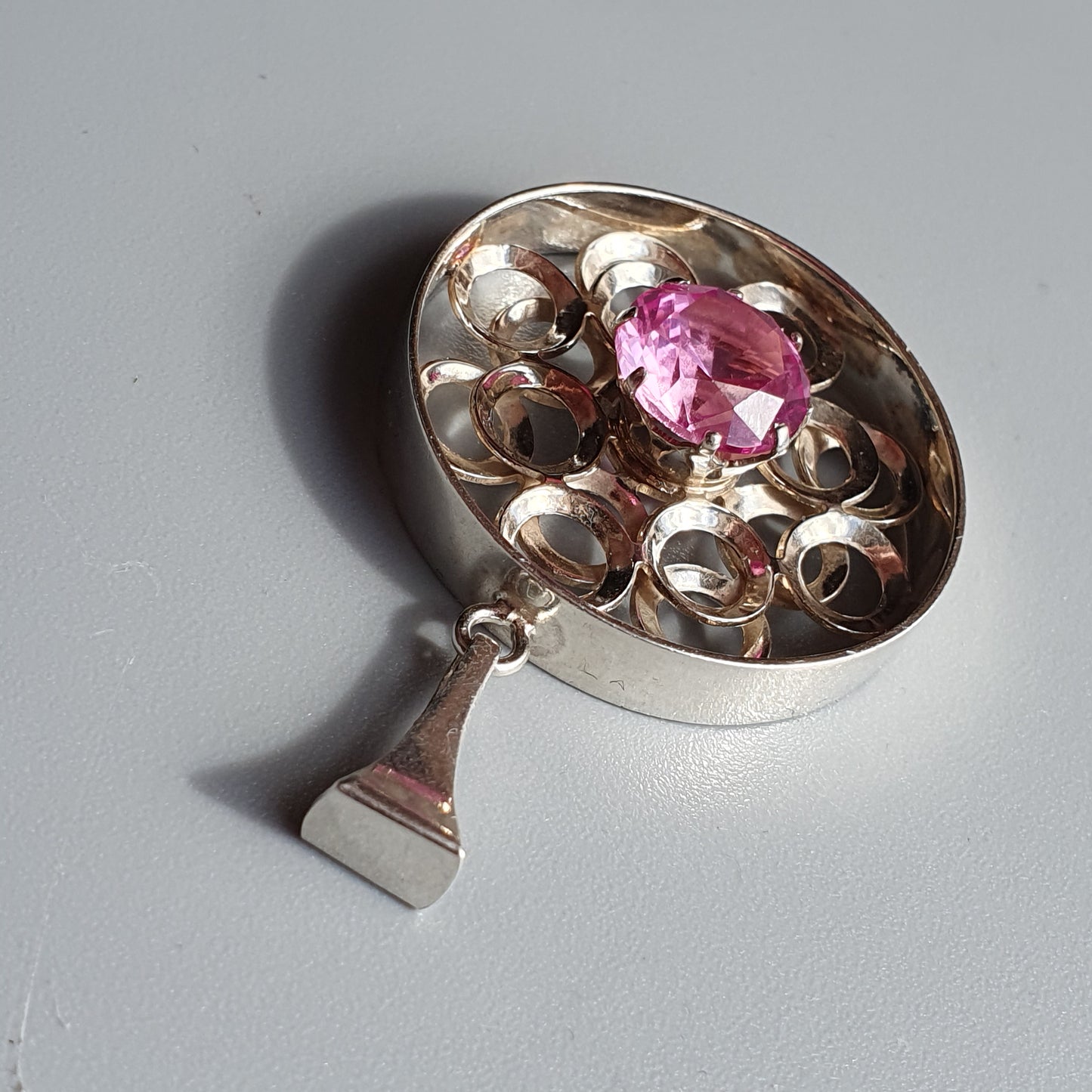 Silver pendant with a pink gemstone surrounded by intricate metalwork.