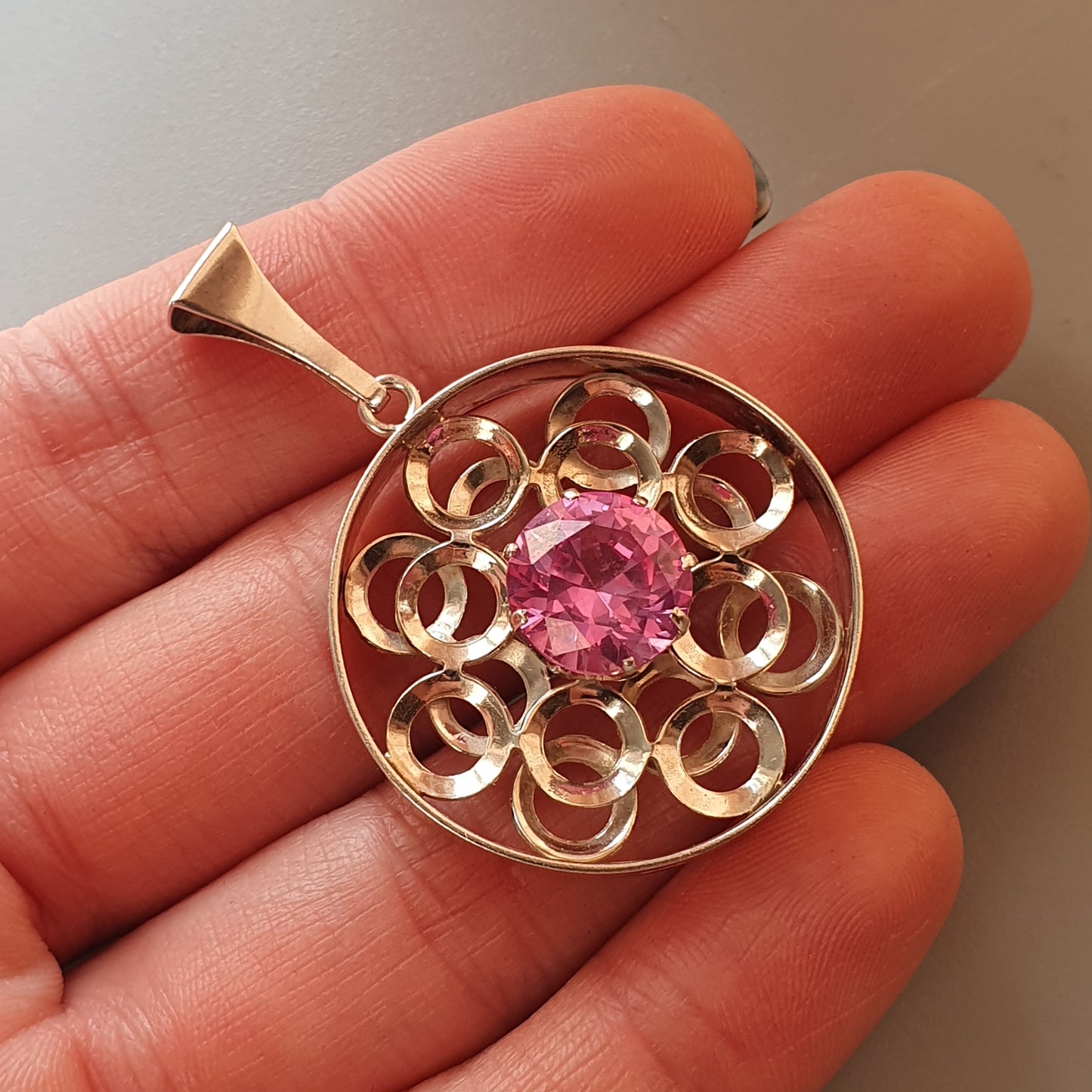 Gold pendant featuring a circular design with spiraling elements surrounding a central pink gemstone.