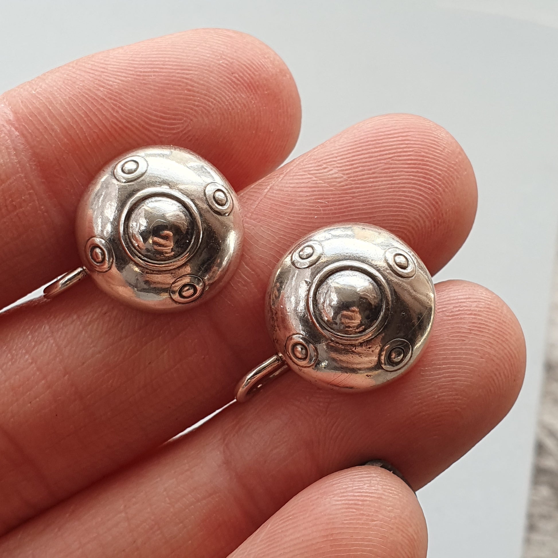 Silver earrings shaped like circular metal discs with raised details.