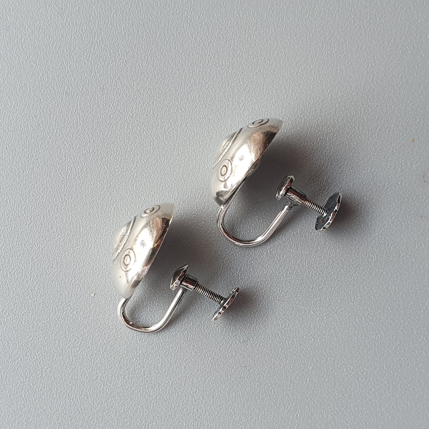 Pair of silver-colored screw-back earrings with a curved, engraved design.