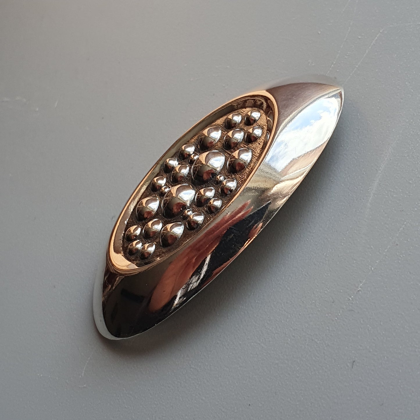 Elongated metallic brooch or pin with a cluster of small beads or studs in its center.