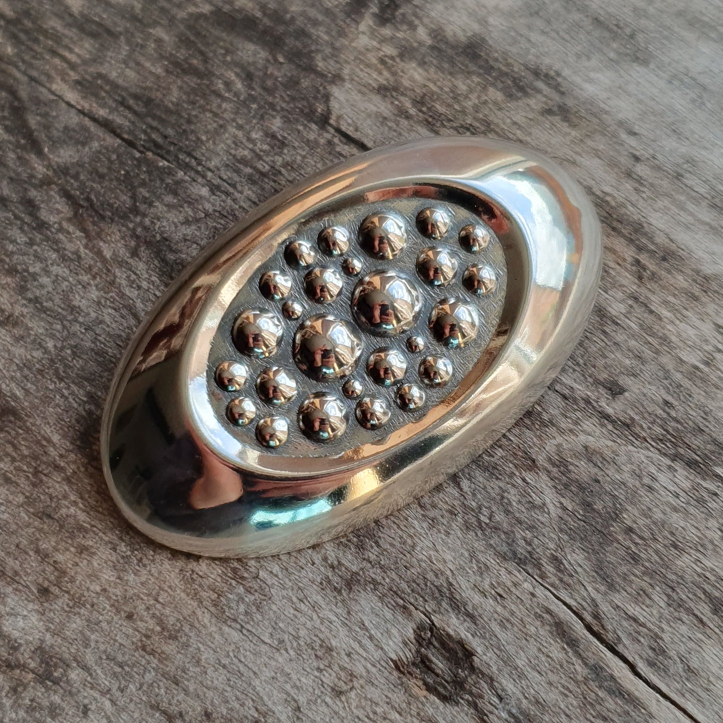 Oval-shaped metallic object with raised spherical bumps arranged in a circular pattern.