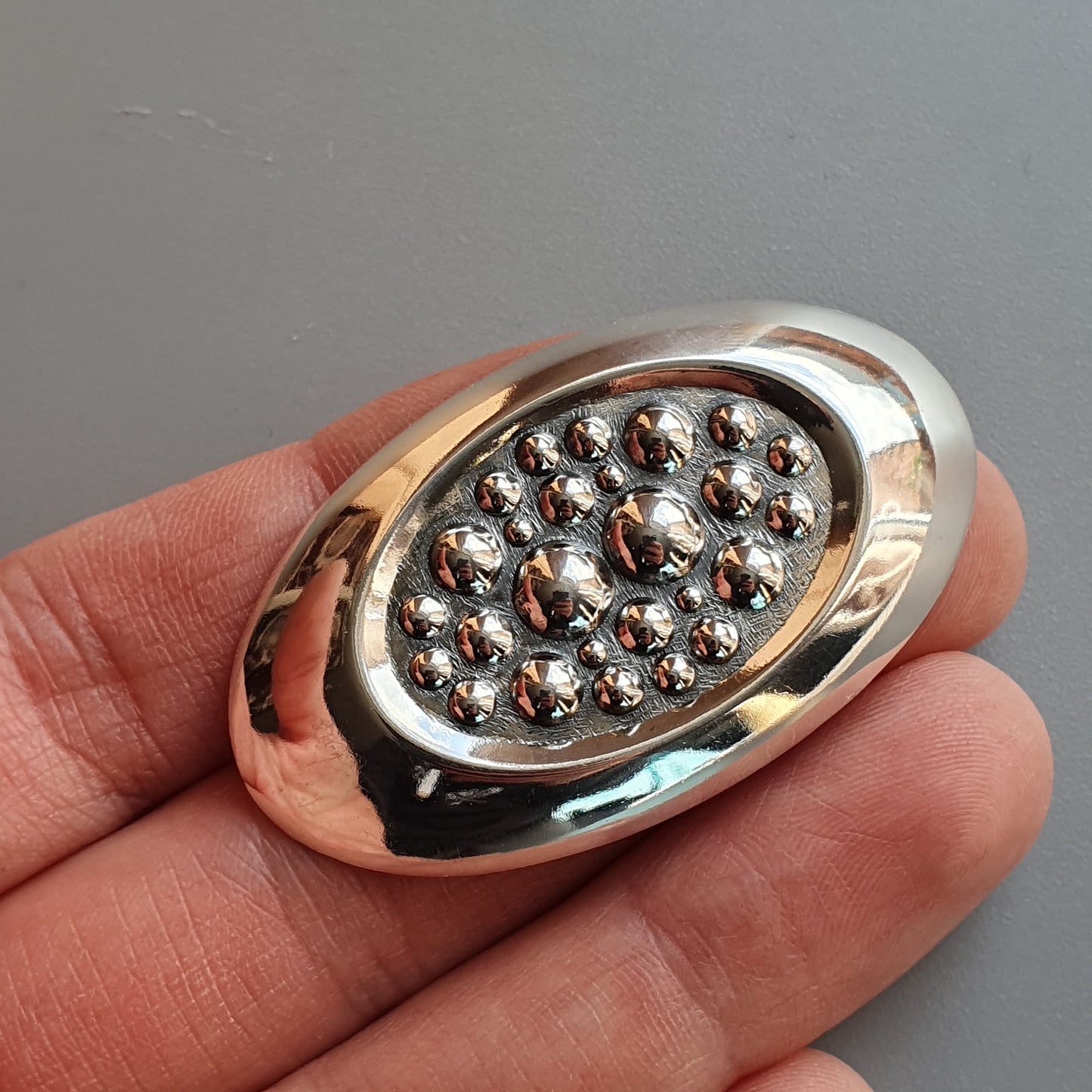 Oval-shaped silver brooch or pin with multiple small metallic spheres arranged in a pattern.