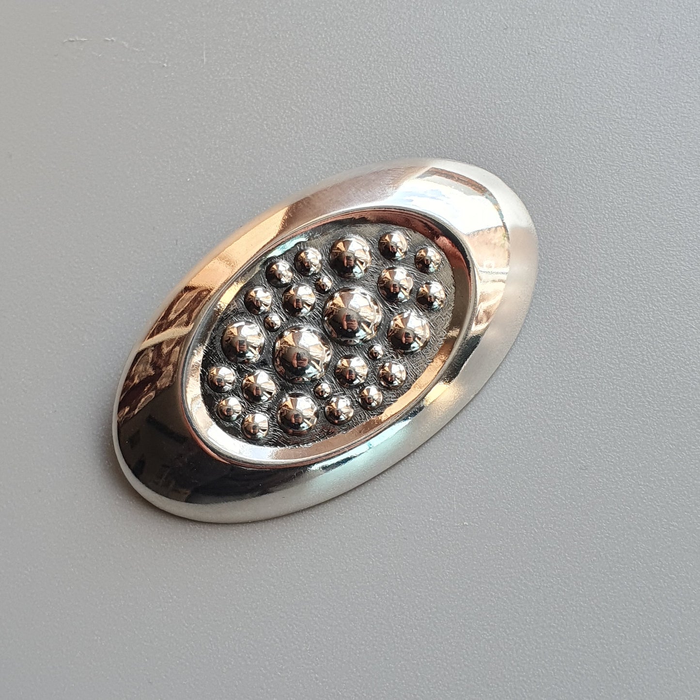 Oval-shaped silver brooch or pin with a cluster of small metallic beads in the center.