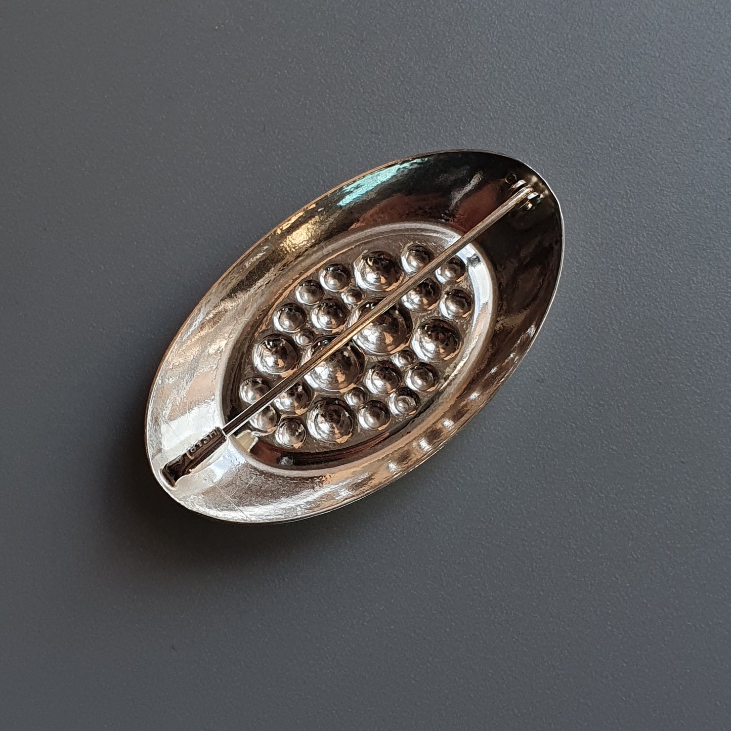 Oval-shaped silver brooch with a pattern of small raised dots.