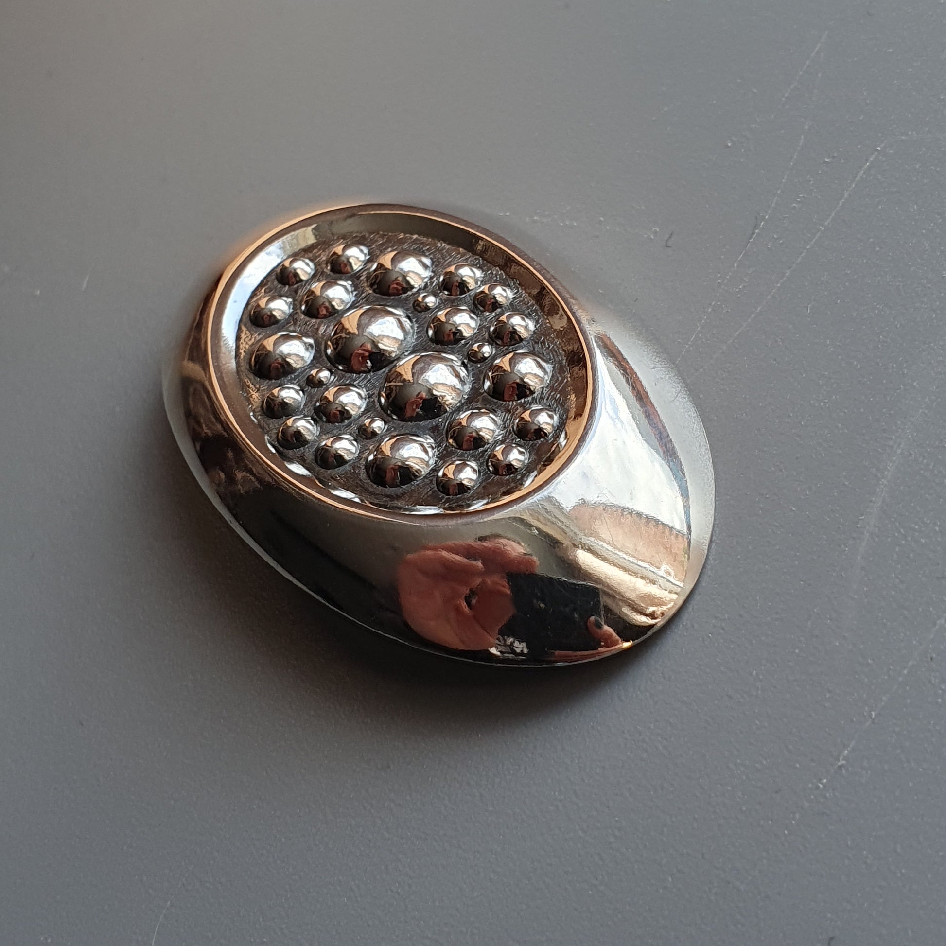 Metallic circular object with a cluster of small silver balls in its center.