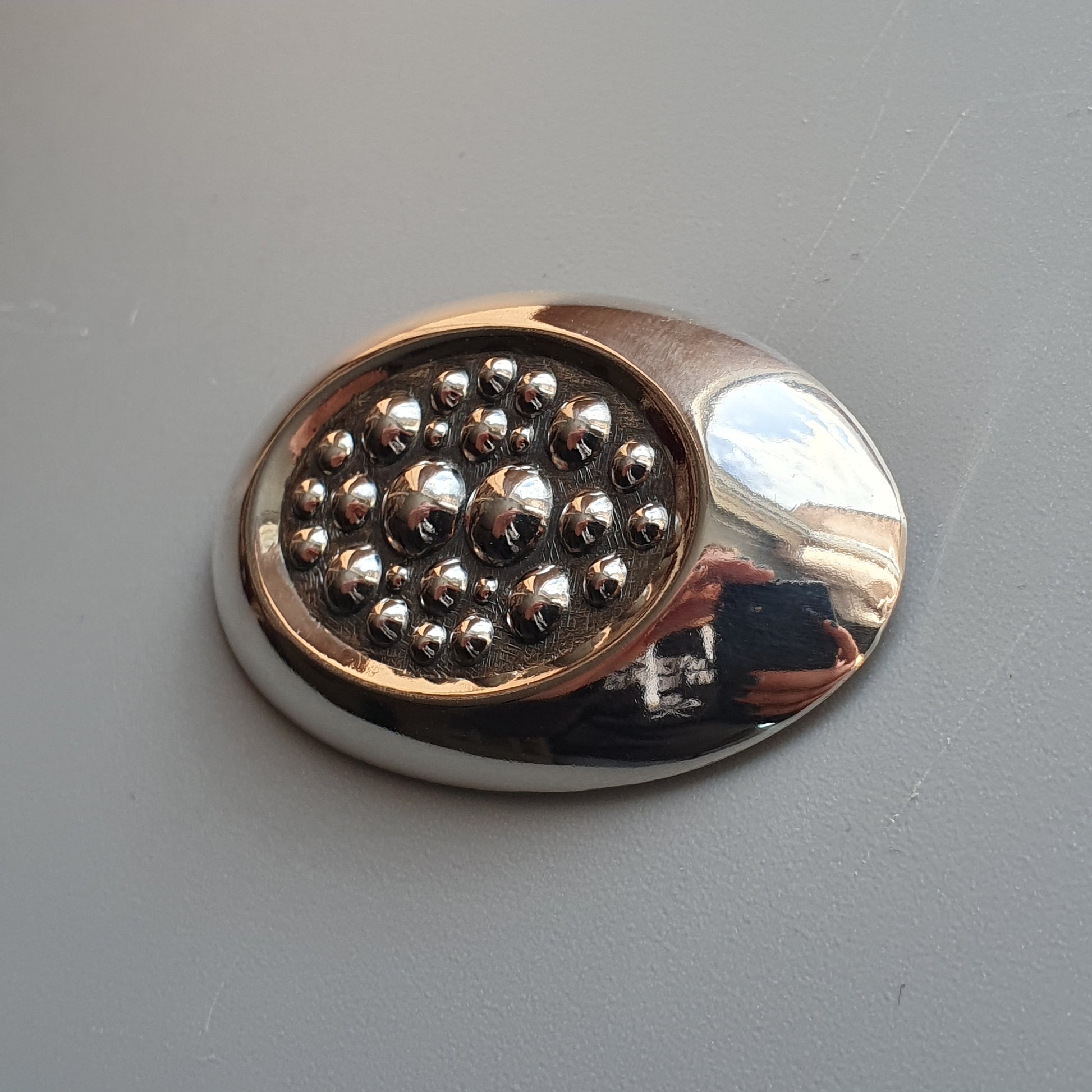 Oval-shaped metallic brooch or pin with a cluster of small spherical beads in its center.